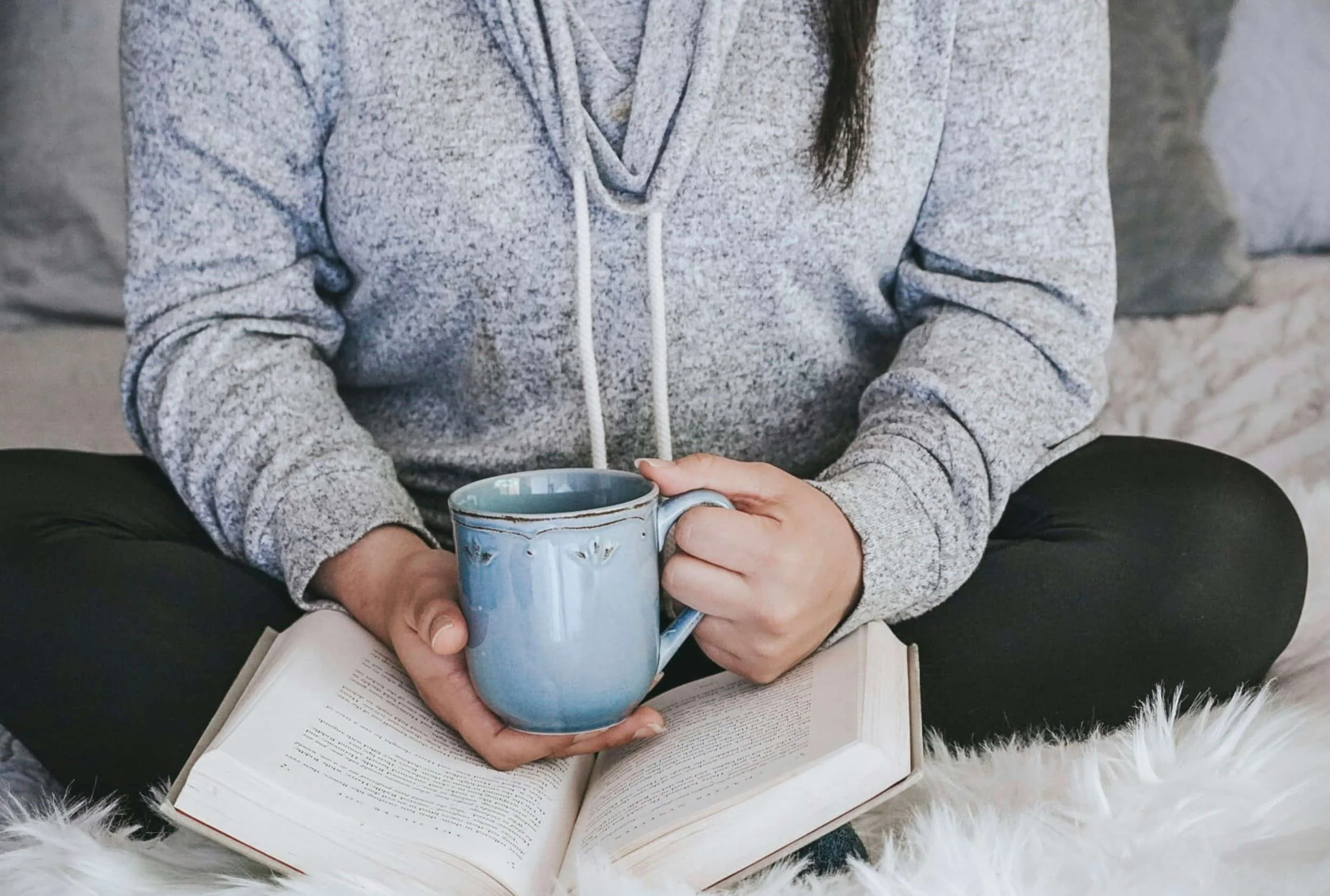 woman in grey hoodie drinking coffee on bed in online unmasking group for autistic women