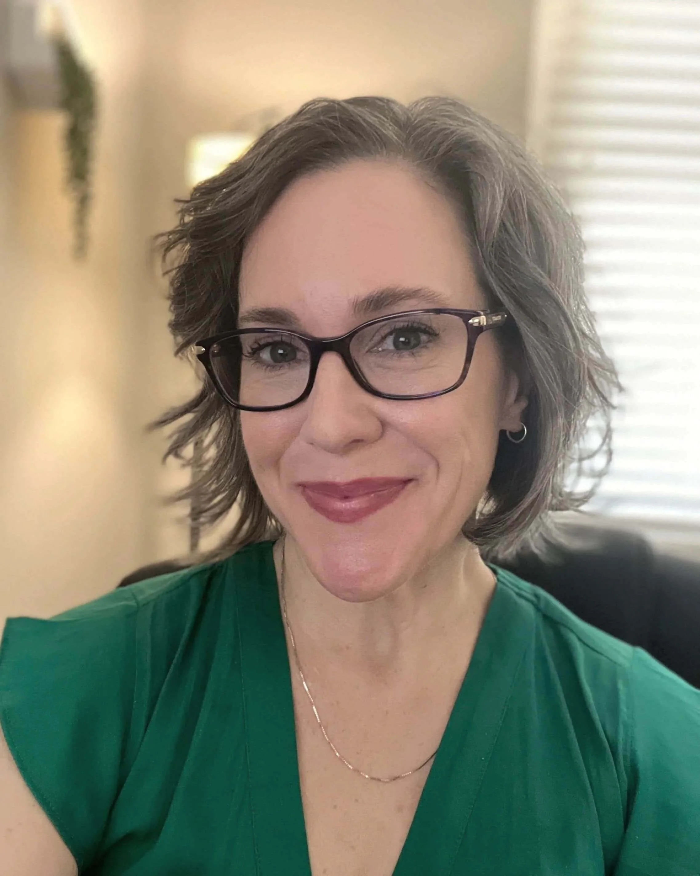 woman with short wavy brown hair and green blouse wearing glasses