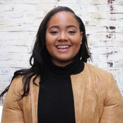 A young woman with medium skin tone and long black hair, wearing a red top and a necklace, smiling against a plain white background.