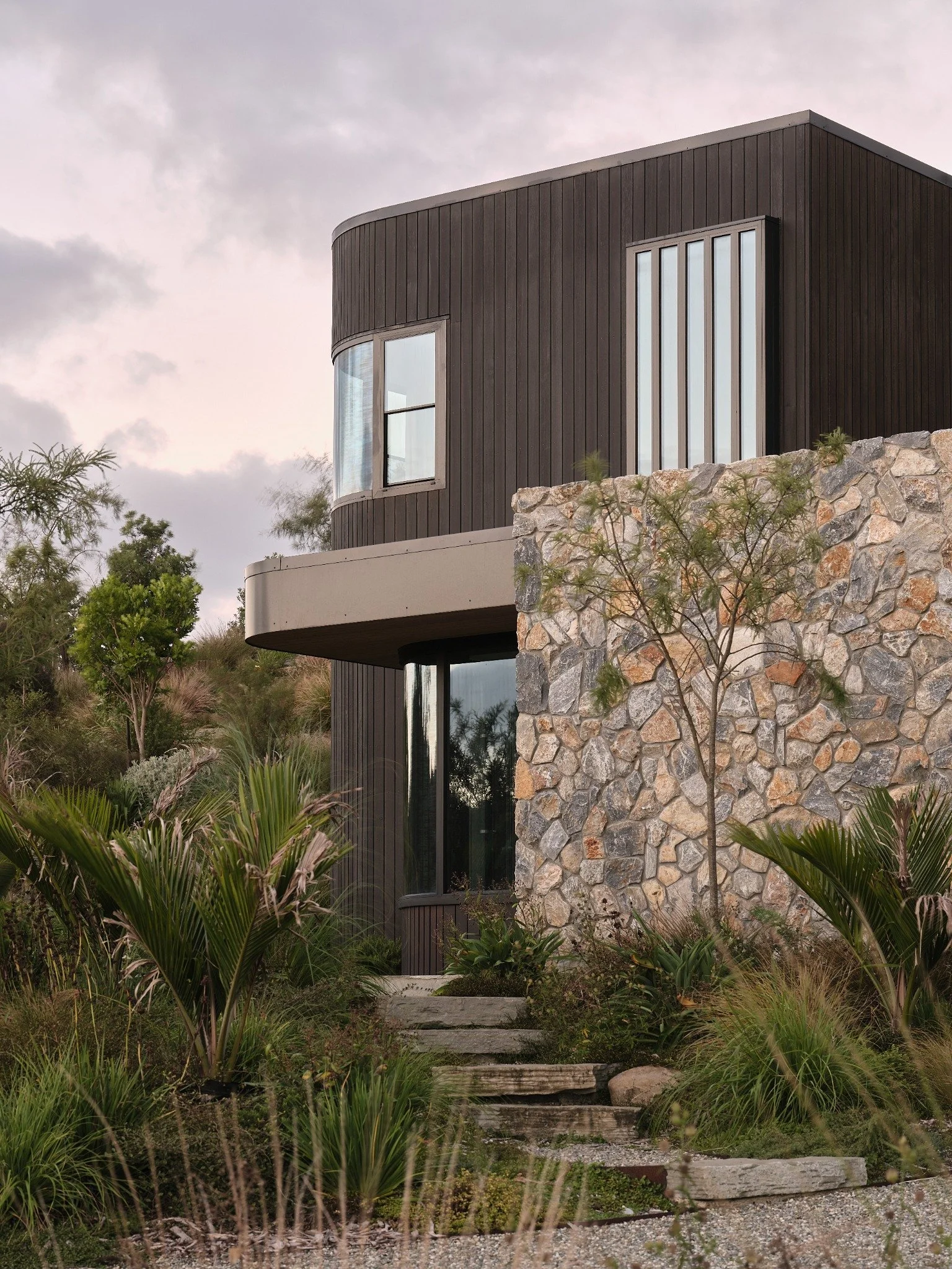 Modern coastal landscape design at Ti Point featuring natural stone cladding, native planting and curved garden beds by Rochford Landscapes.