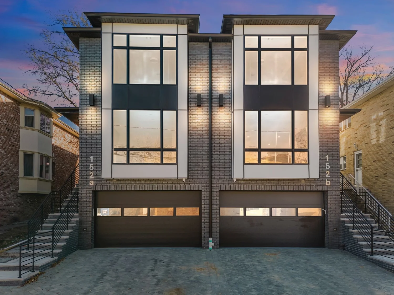 152 Morningside: two attached homes at dusk with lit windows and garage doors