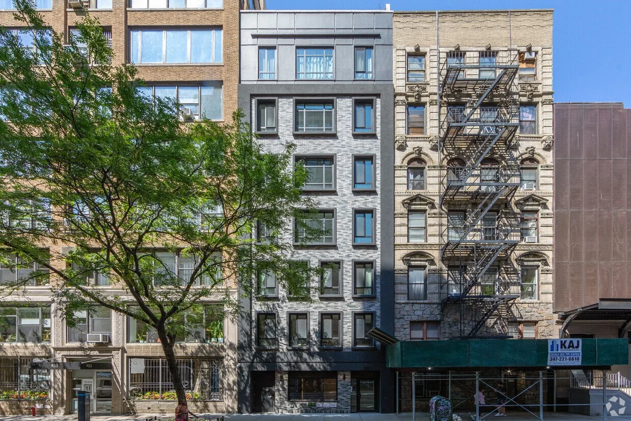 231 West 26th St: a gray multi-story residential building with a fire escape on a tree-lined street