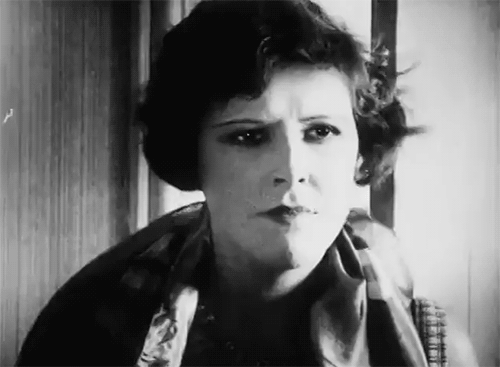 Black and white photograph of a woman with short, curly hair staring with a confused or skeptical expression.