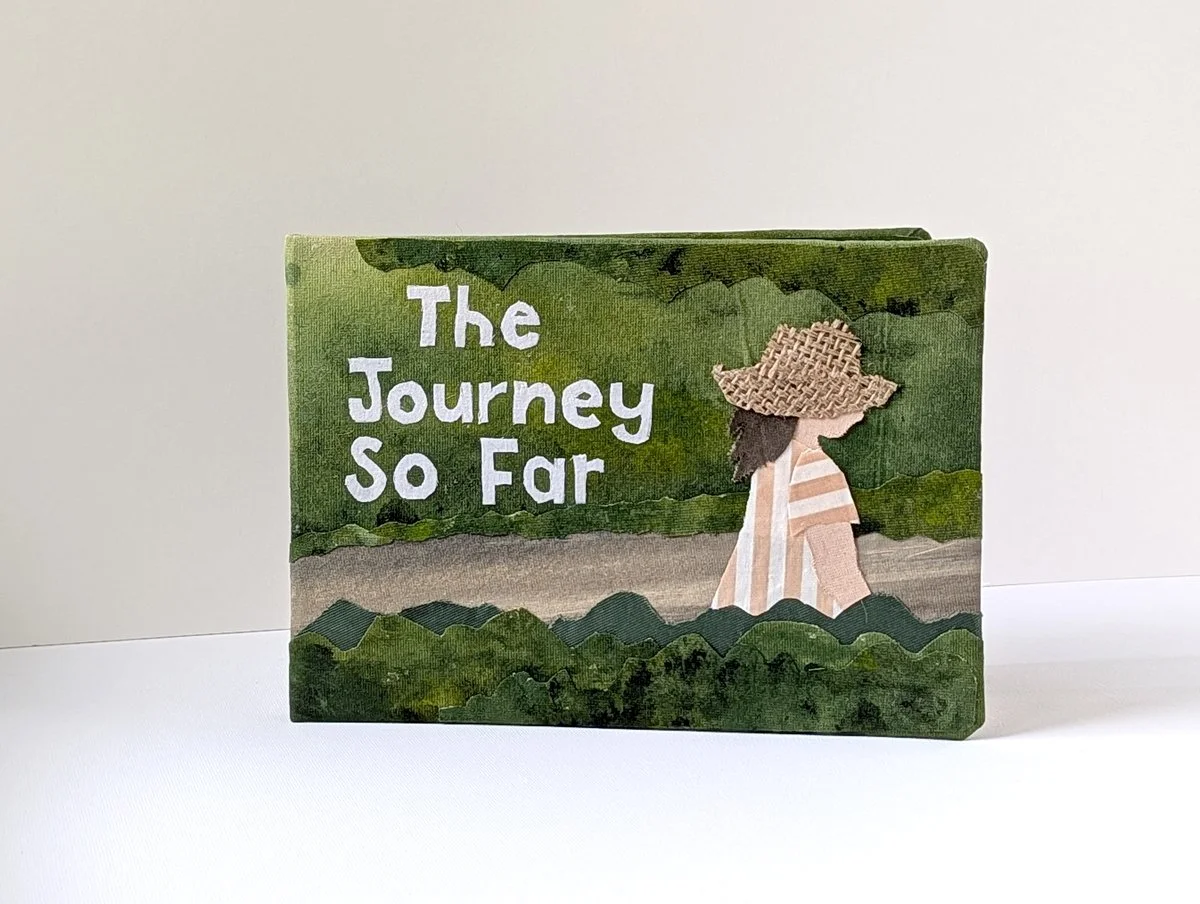 Book titled 'The Journey So Far' with an illustration of a woman wearing a large straw hat and a striped dress, walking through green foliage.