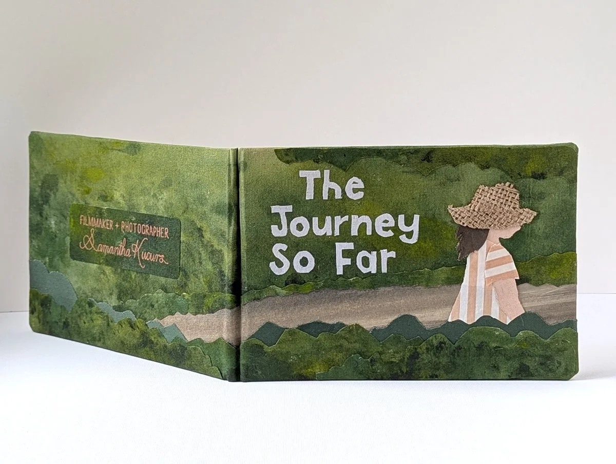 Open illustrated book titled 'The Journey So Far' with a woman wearing a wide-brimmed straw hat and striped dress, walking through a green forest setting.