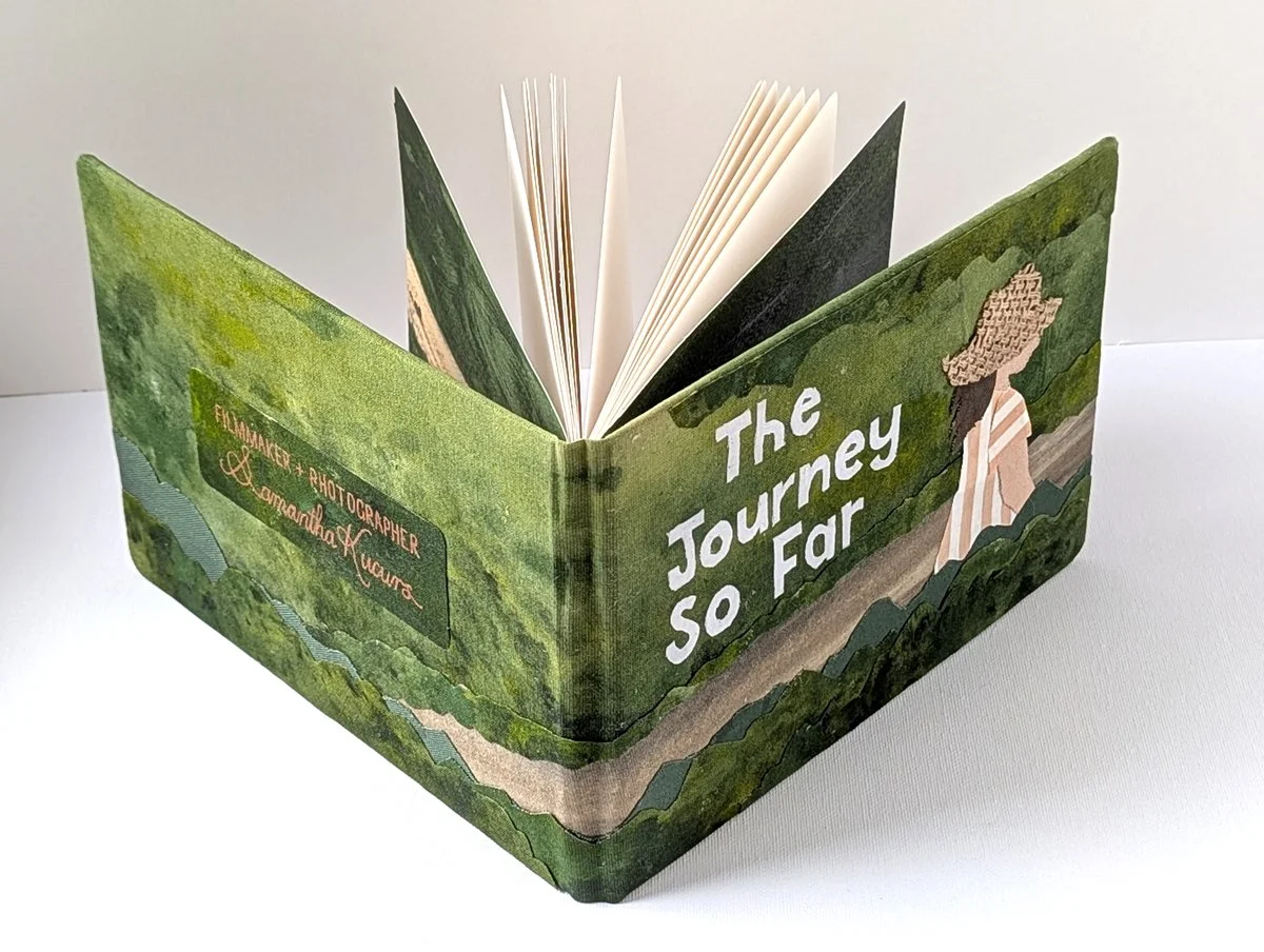 Open illustrated book cover titled "The Journey So Far" with a woman in a dress and floral hat walking on a path through green trees.