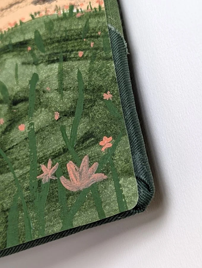 Close-up of a illustrated notebook cover featuring green grass and pink flowers.
