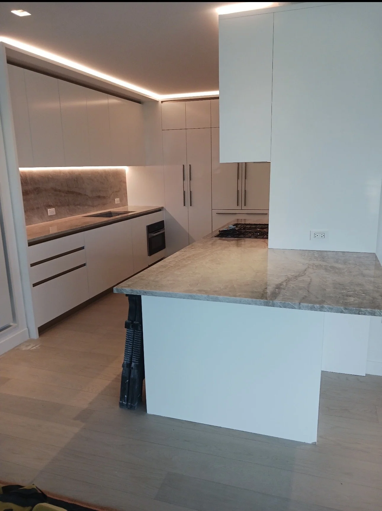 Modern kitchen with white cabinets, marble countertops, and a built-in oven, featuring under-cabinet lighting.