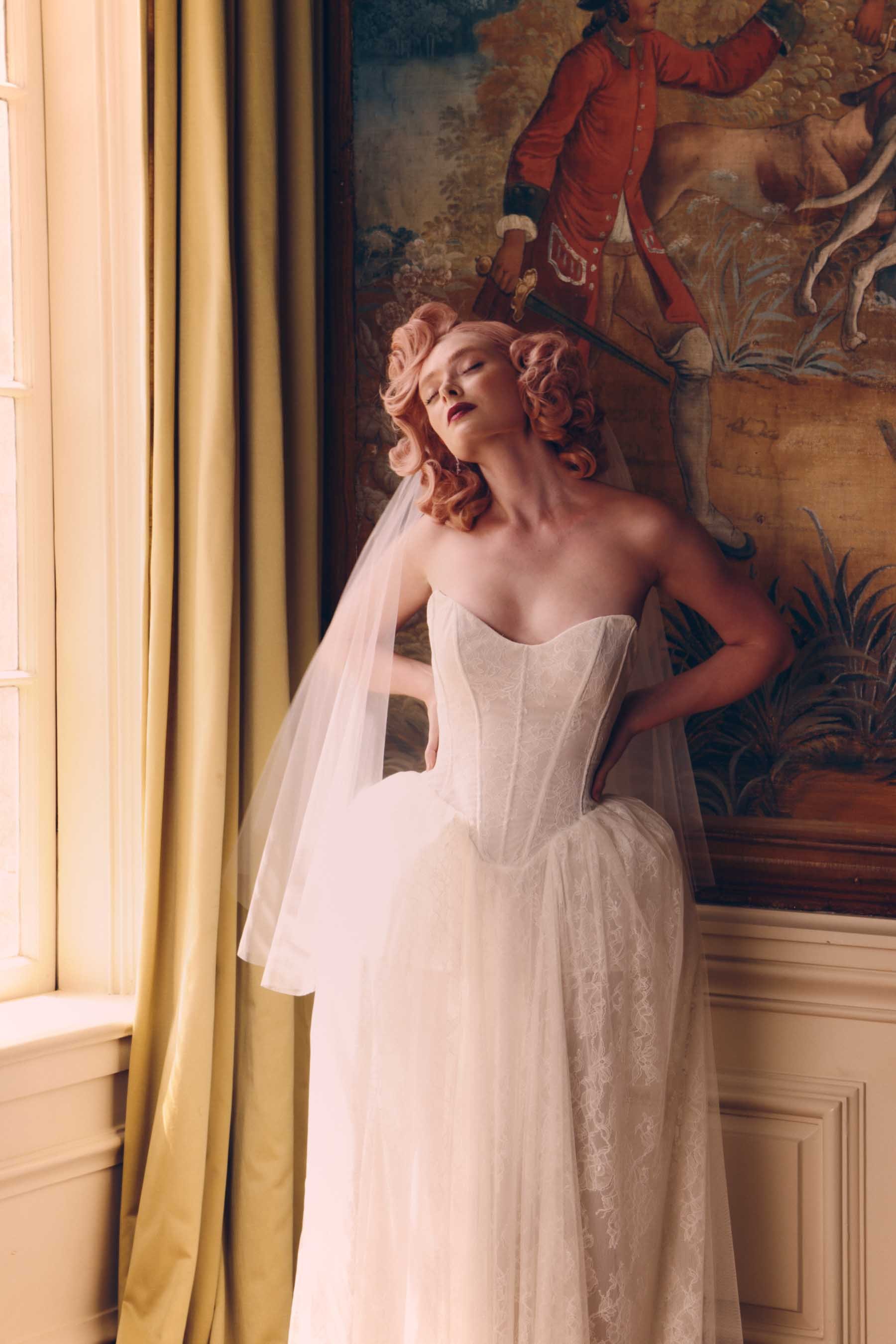 A woman wearing an elegant off-the-shoulder white satin dress with beaded details on the neckline, holding her hands near her hips, against a plain background.