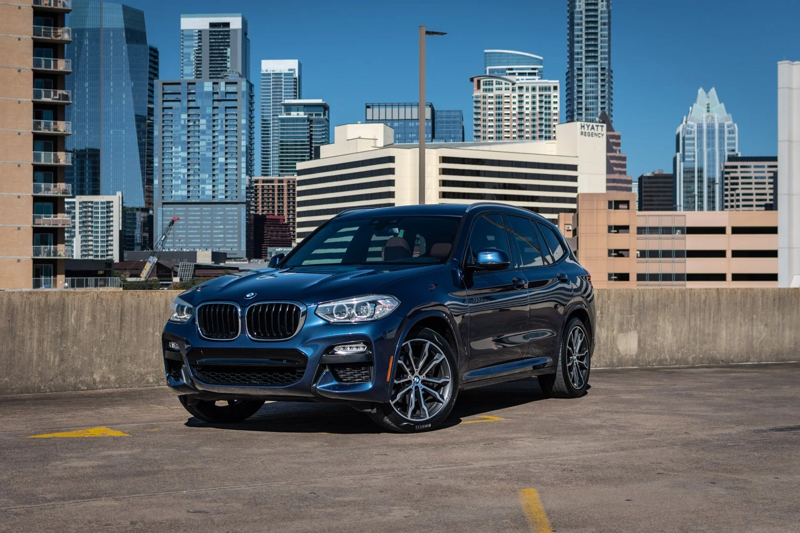 A black BMW SUV parked on the top level of a parking garage with a city skyline in the background.