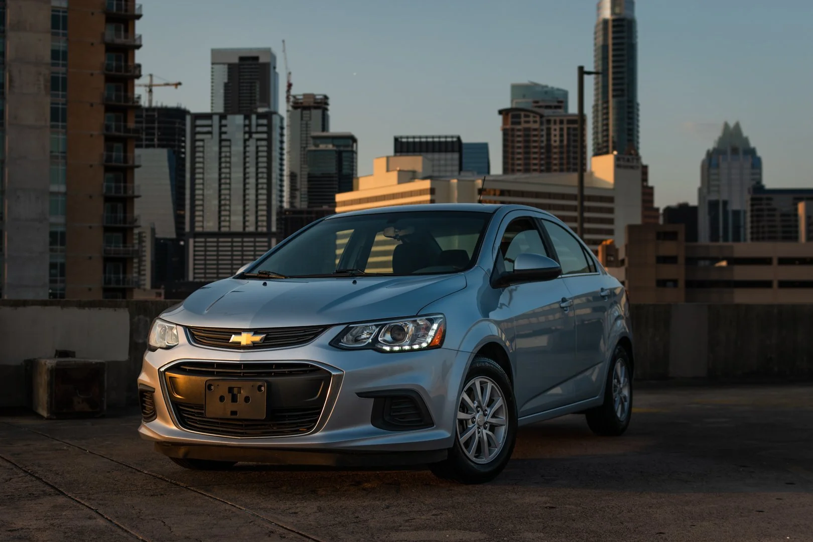 A silver Chevrolet sedan parked on a rooftop parking lot with a city skyline in the background during sunset.