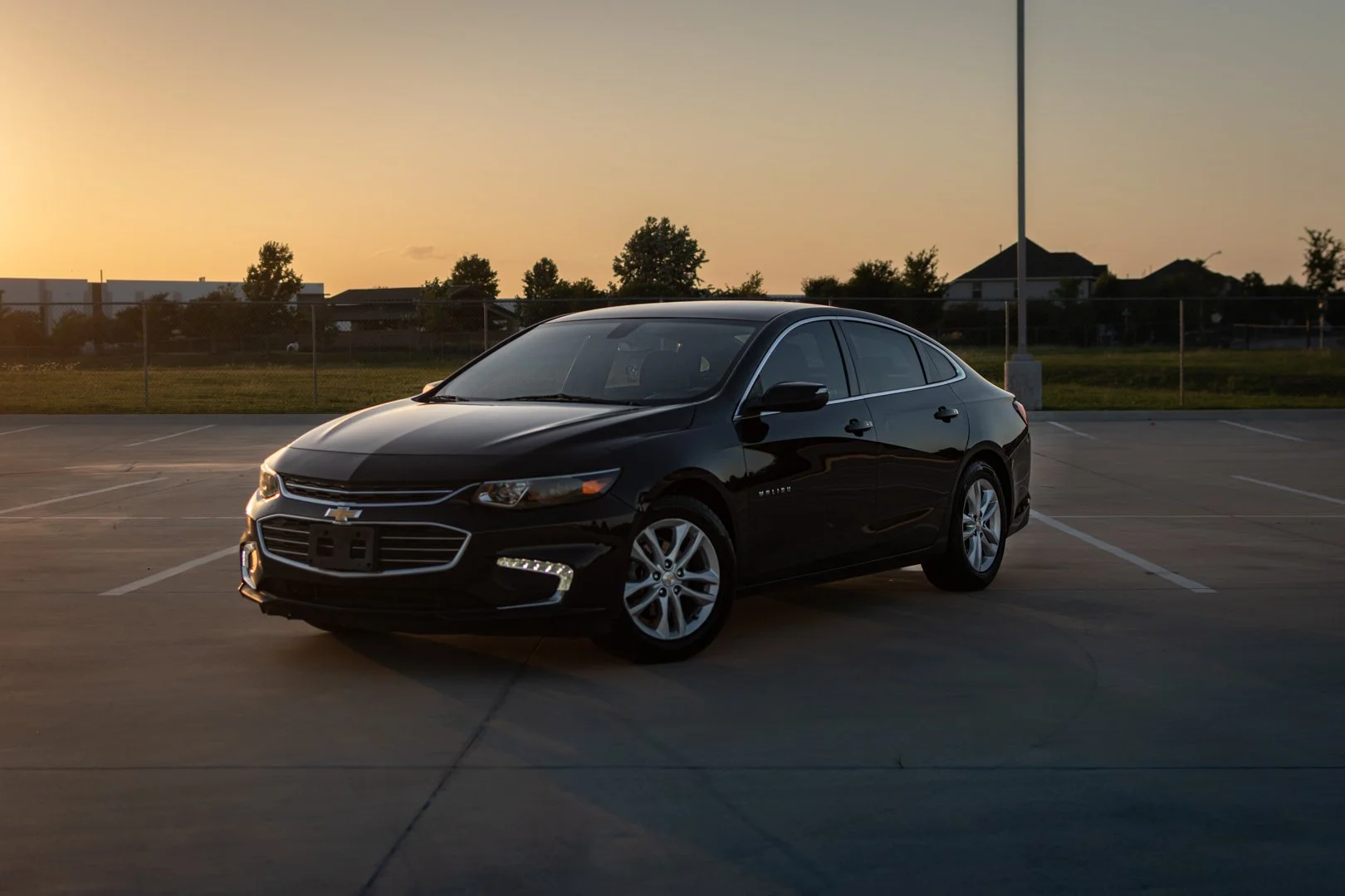 A black Chevrolet sedan parked in an empty parking lot during sunset.