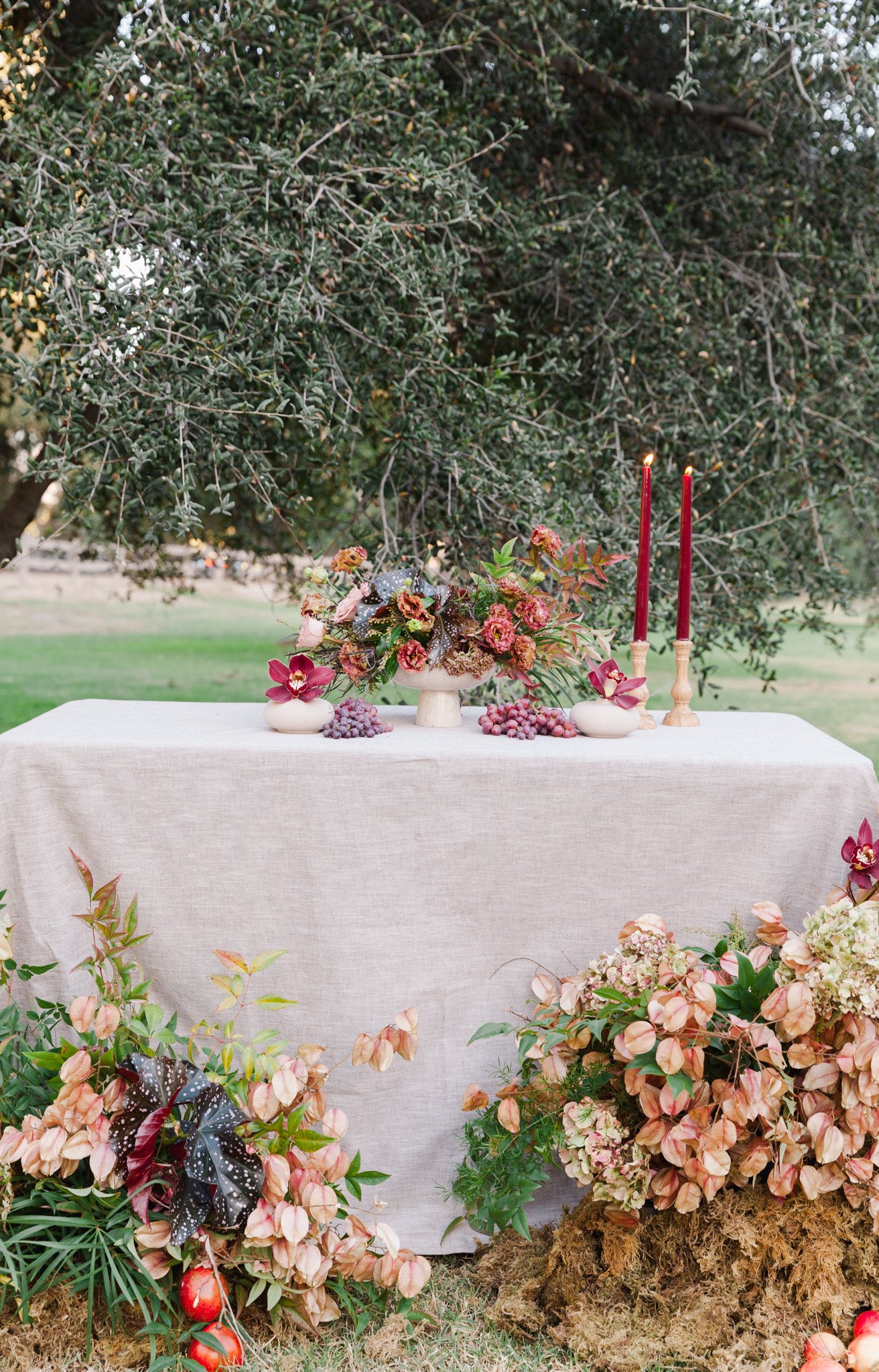 A fall flower tablescape in Los Angeles using grapes, candles, pomegranates, brown, purple, orchids, grapes