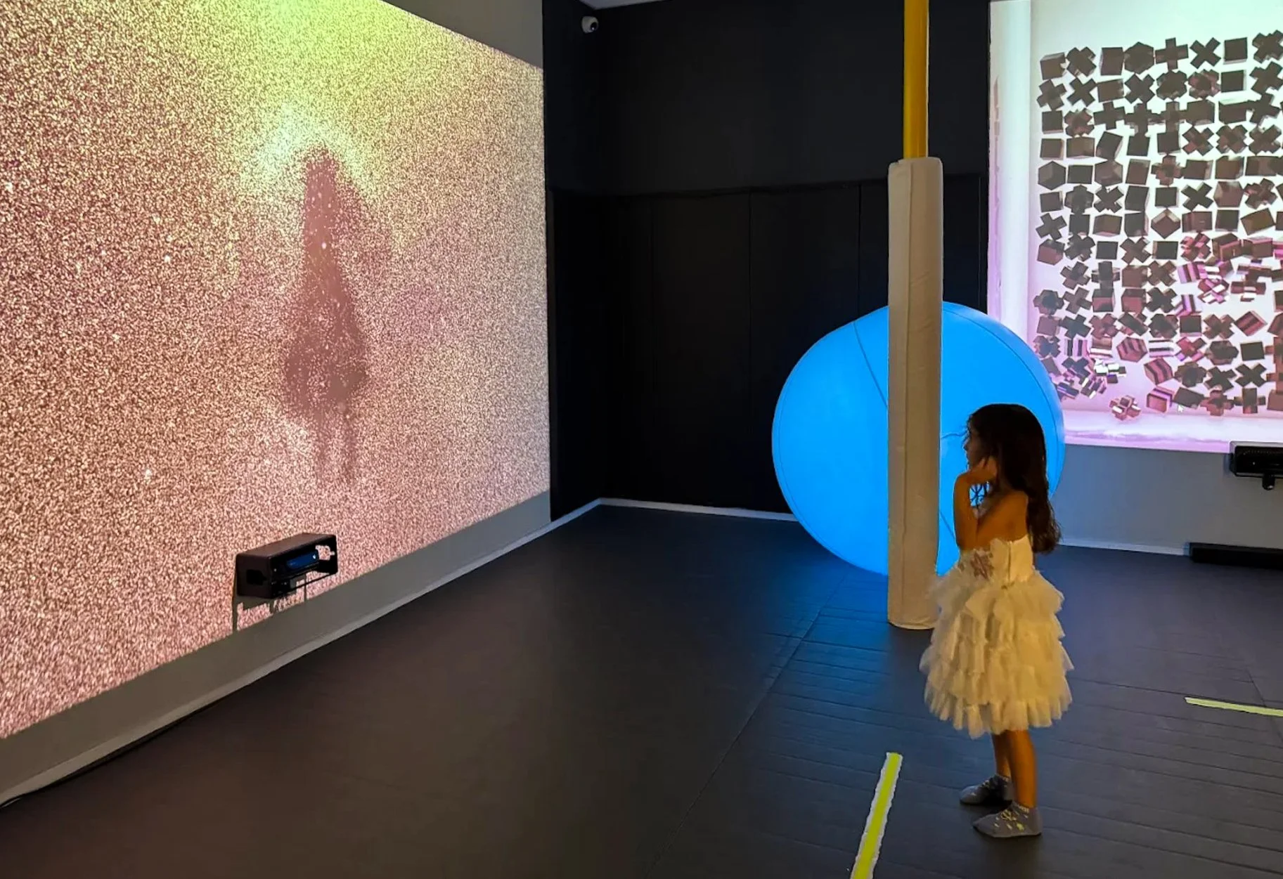Interactive play projectors in dark room with colorful light balls, with a girl in middle of the room dancing and playing game.