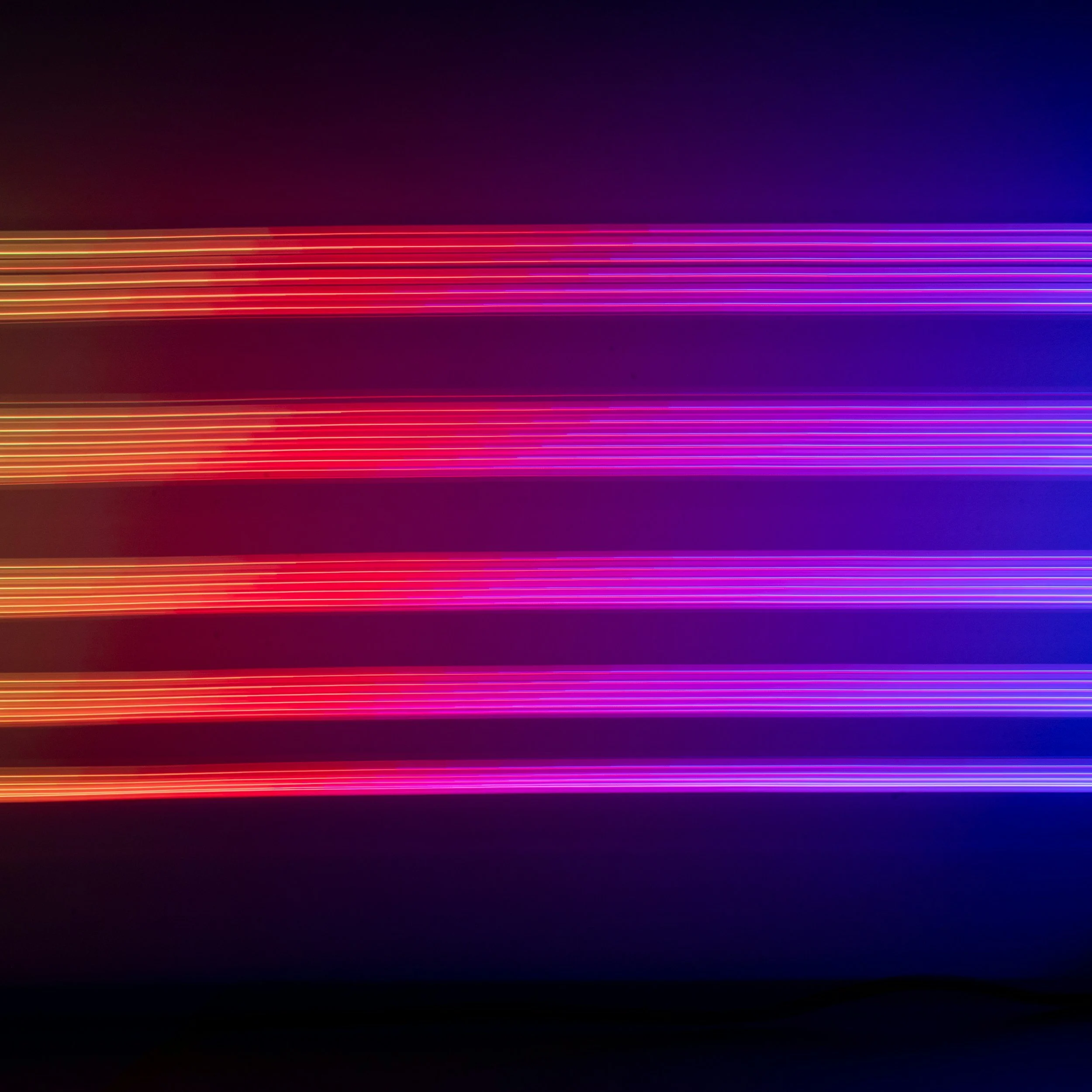 Lignes colorées de lumière fluide en dégradé de rouge, violet et bleu sur fond sombre.