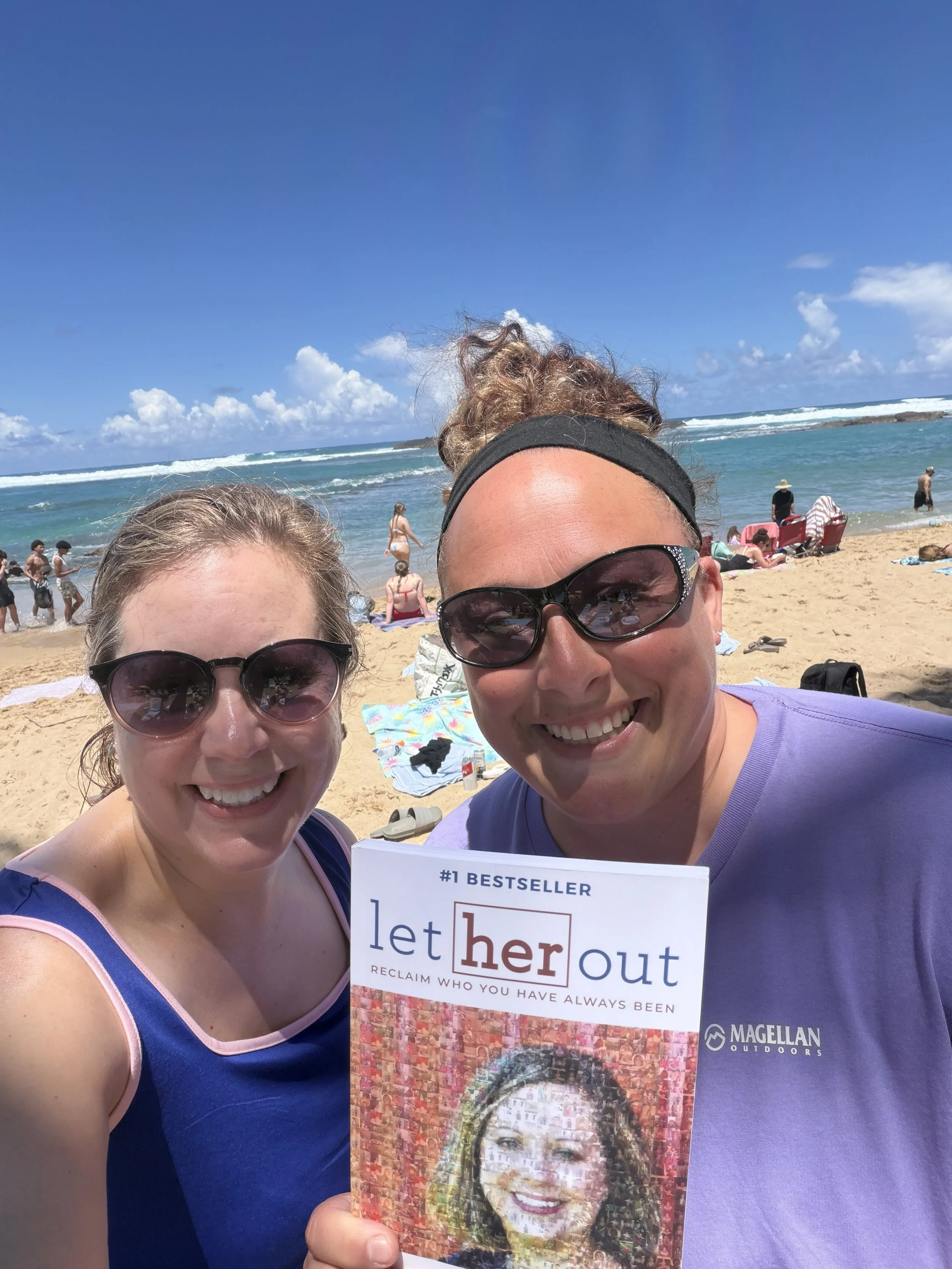 Two women smiling together on a beach in Puerto Rico with palm trees, sand, and ocean water in the background during their first in-person meeting after working together virtually for a year.