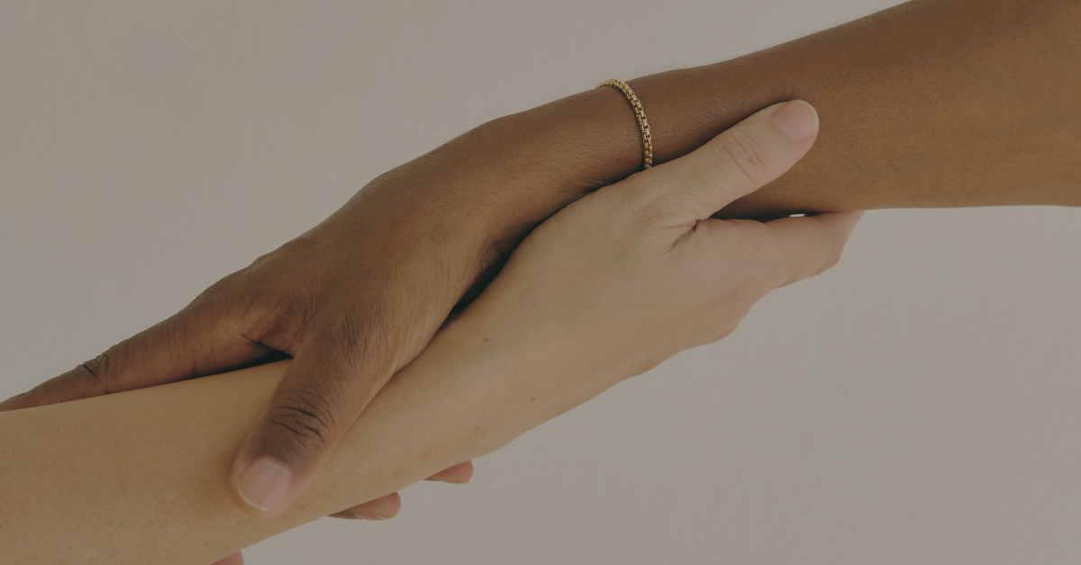 Two hands, one dark-skinned and one light-skinned, holding each other's wrists gently.