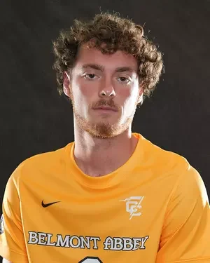 Young man with curly hair wearing a yellow sports jersey with Belmont Abbey logo
