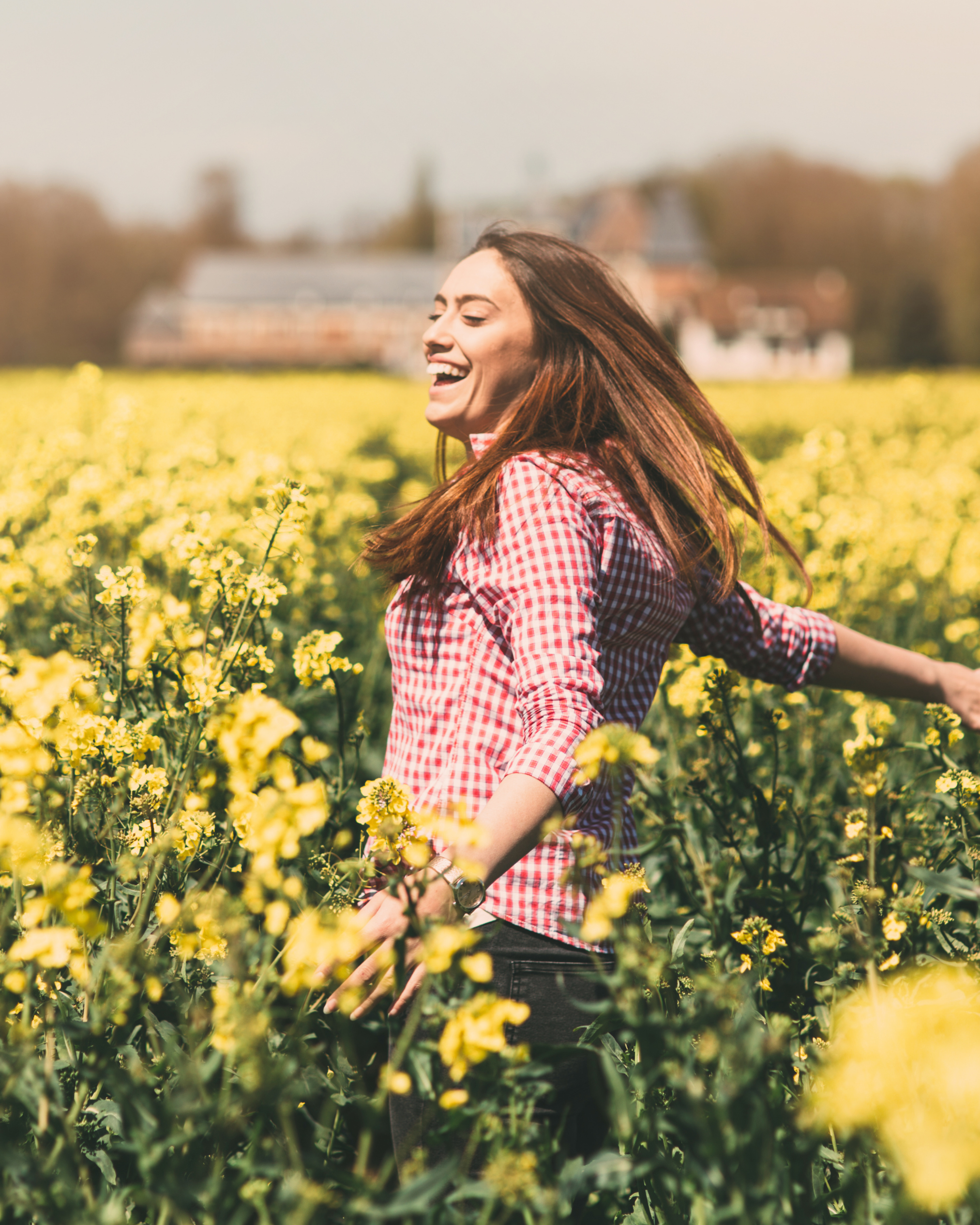 A woman with long brown hair smiling in a yellow flower field feeling peaceful, empowered, and free.