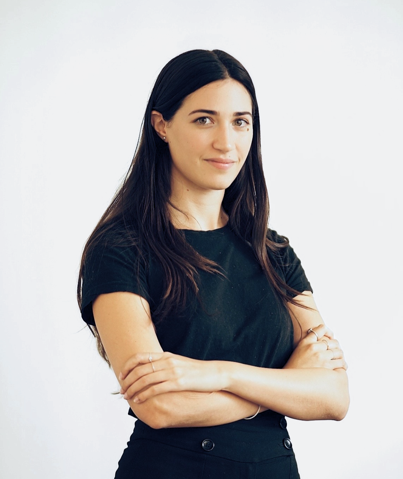 A woman with long, dark hair, wearing a black t-shirt and black high-waisted pants, standing against a plain white background.