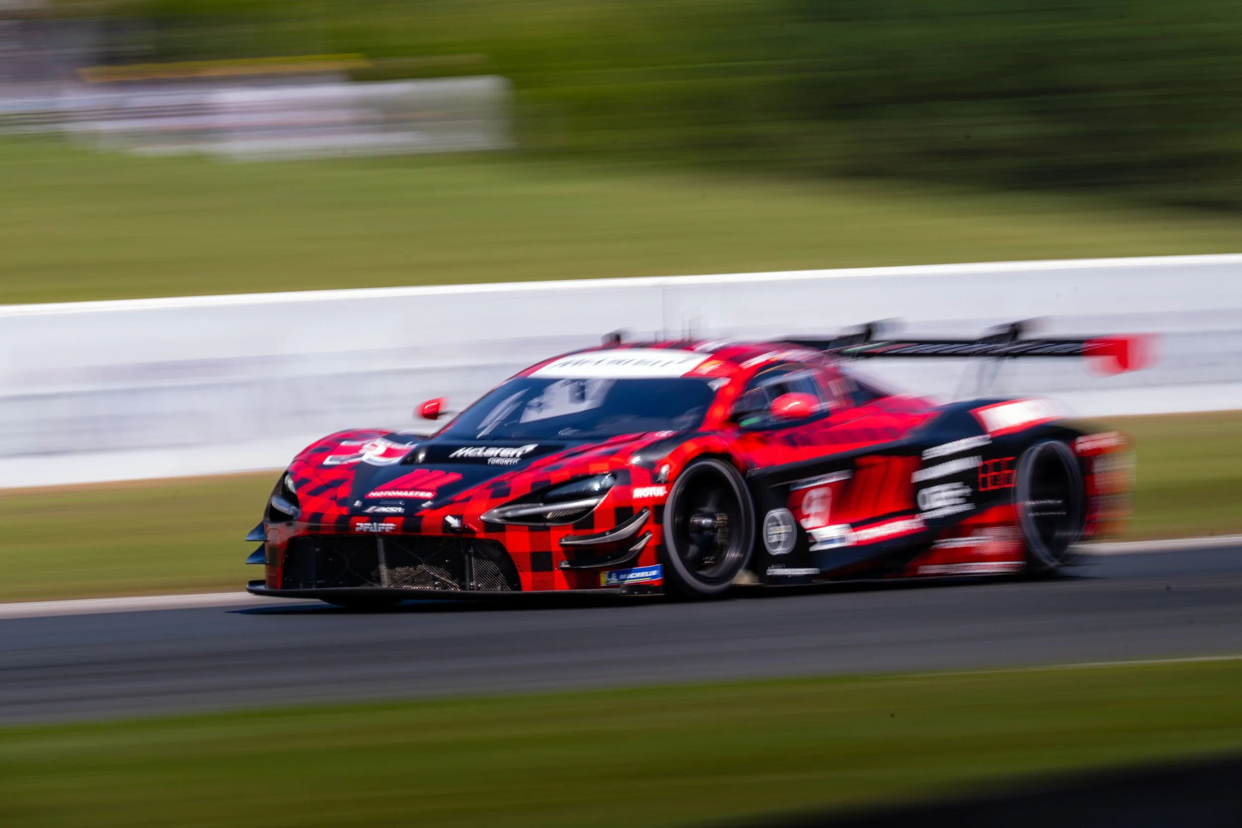 A red and black race car speeding on a racetrack with motion blur in the background.