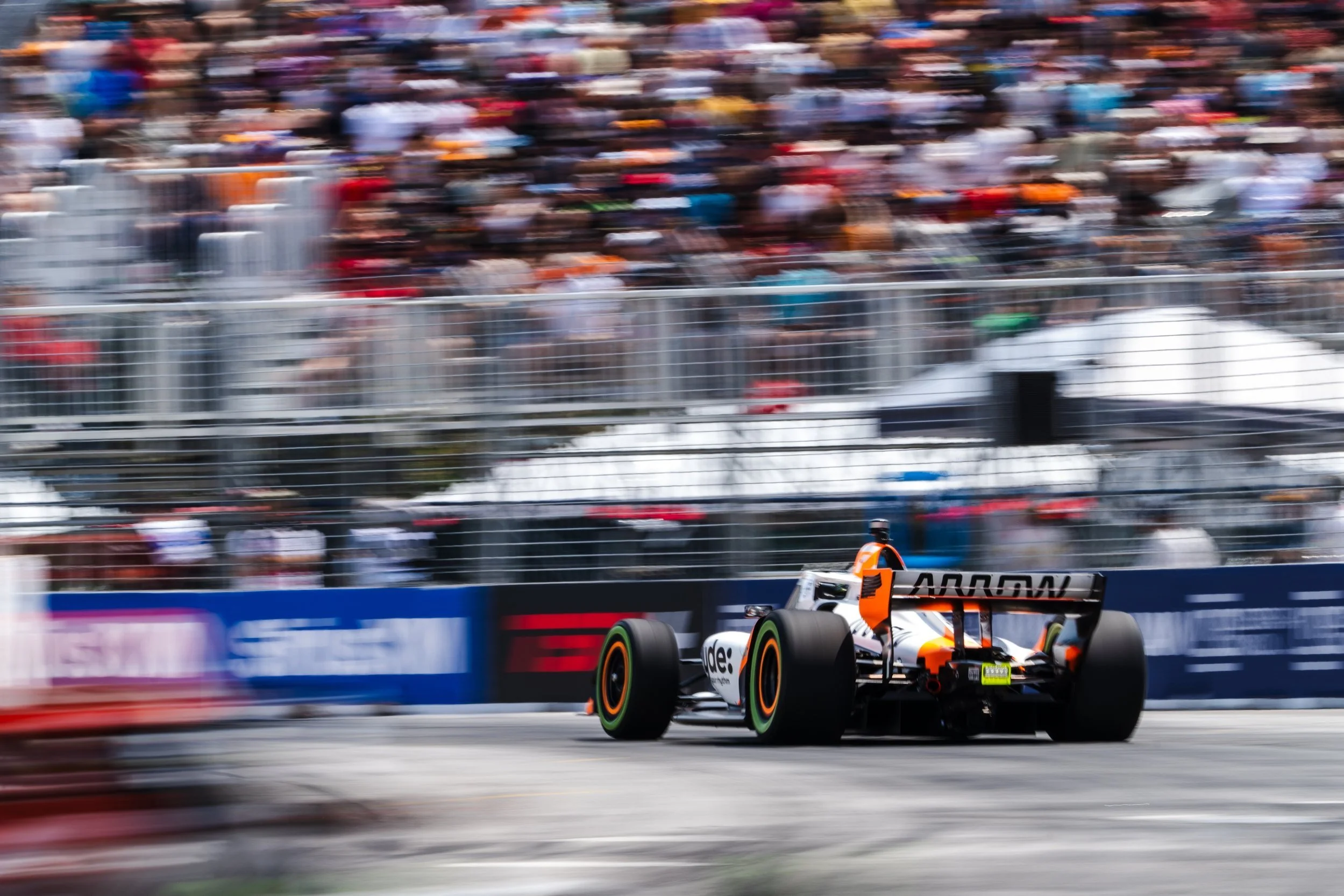 Indycar racing on the streets of toronto with the crowd blurred in the background.