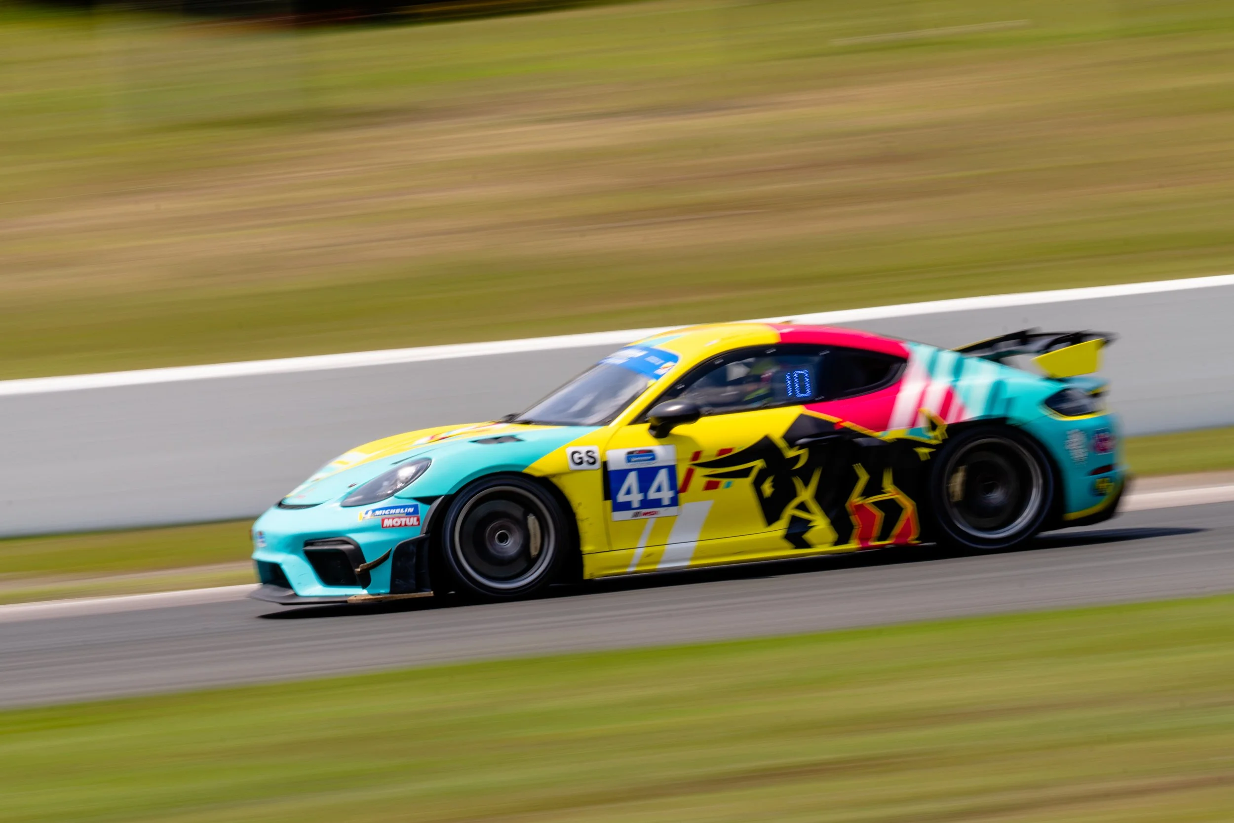 A colorful race car speeding on a track, with a vibrant livery featuring a black horse silhouette and the number 44 on the door.