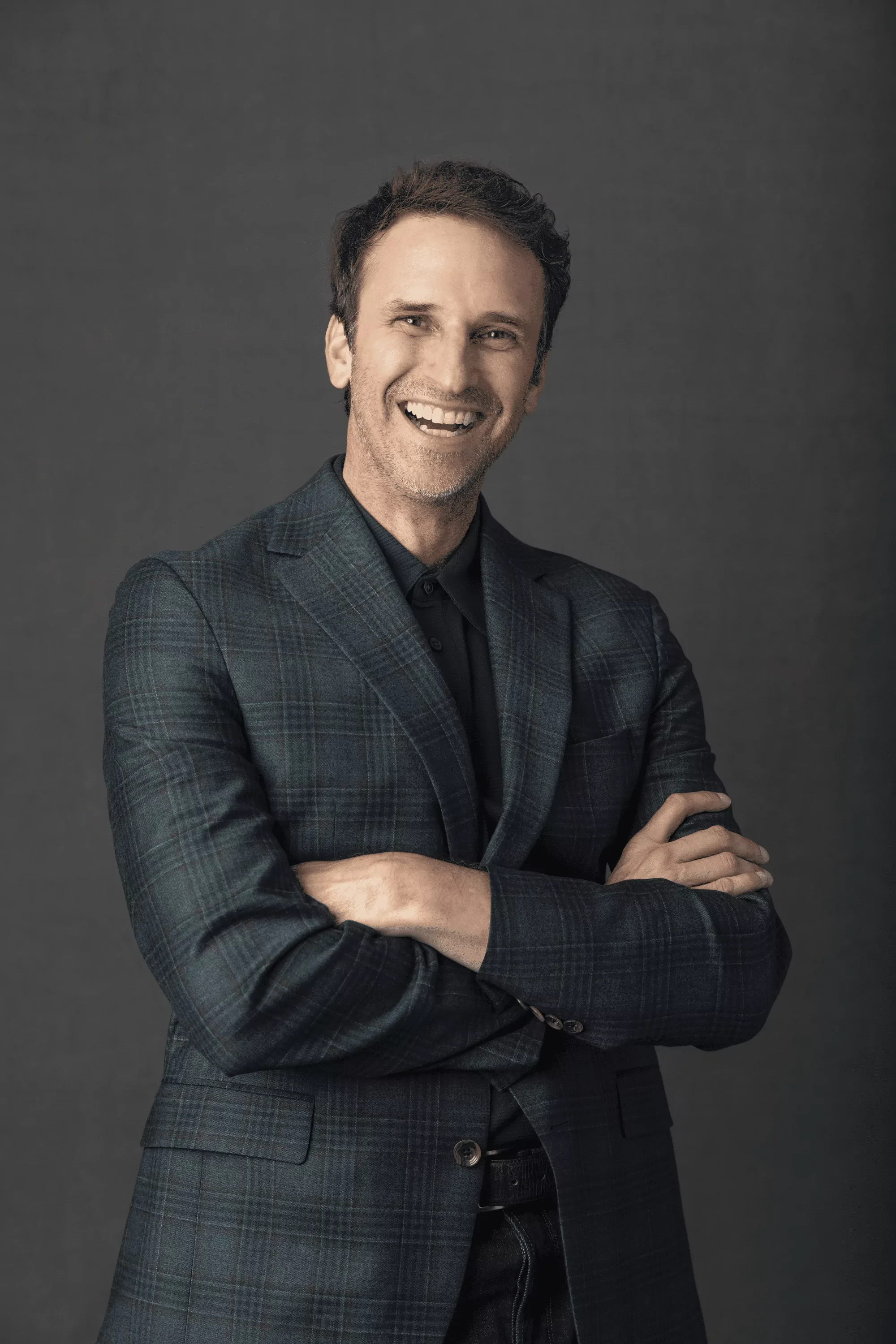 Jeff Salzenstein in a dark plaid blazer with crossed arms standing against a dark grey background.