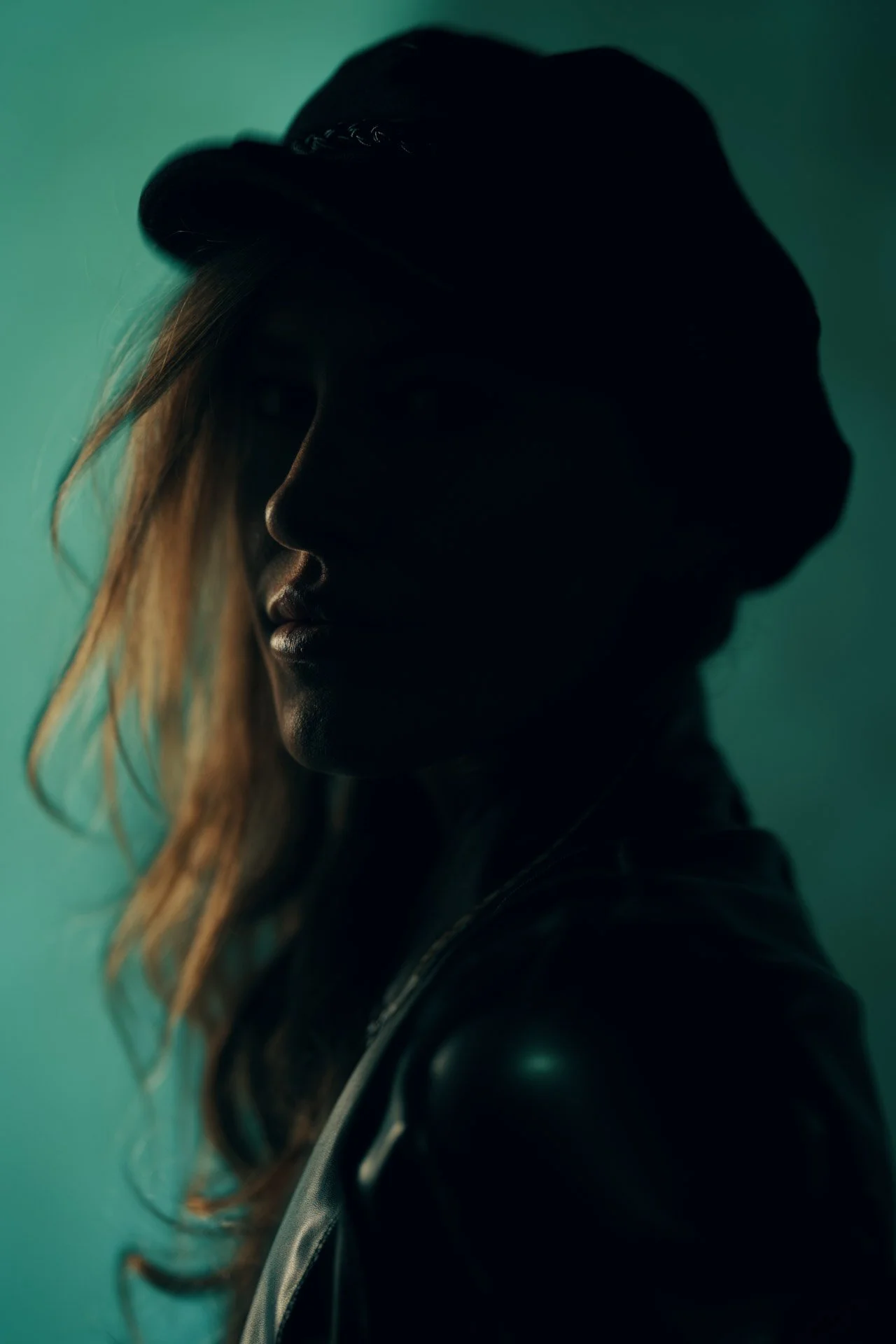 Backlit silhouette senior portrait in a ball cap against a teal studio background