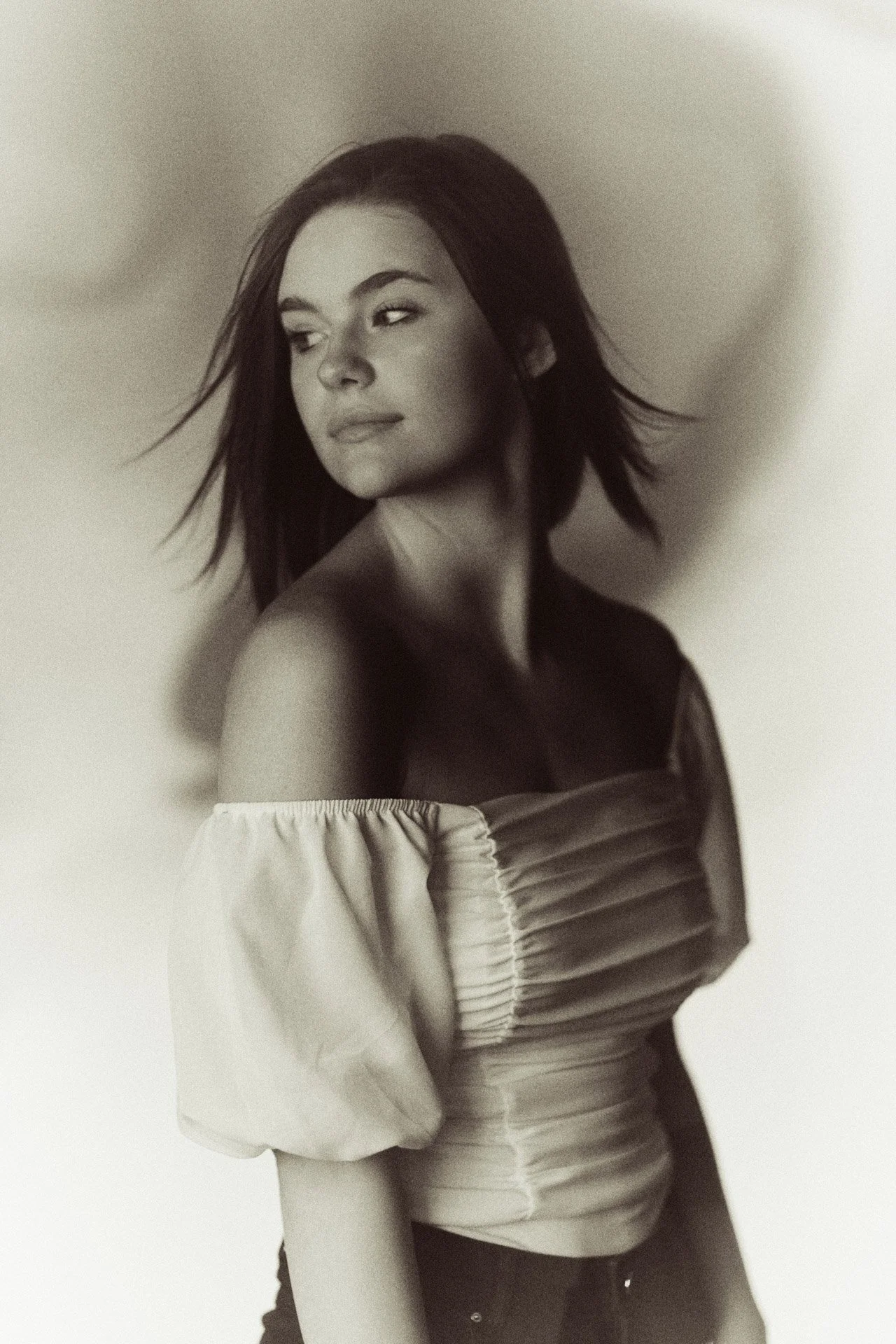 Soft-focus black and white senior portrait of a high school senior in a white puff-sleeve top