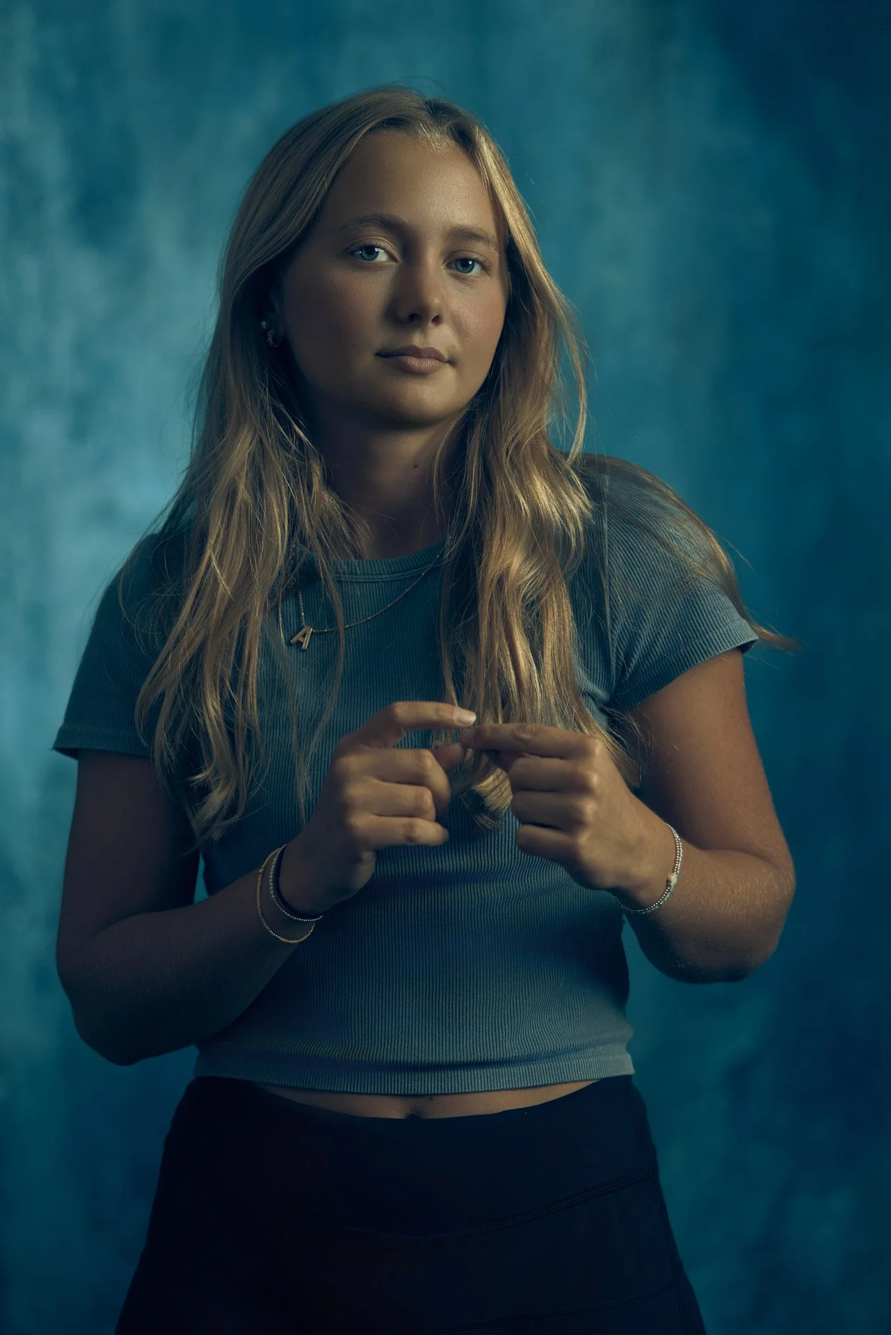 High school senior photographed against a deep teal studio backdrop at The Portrait Lab