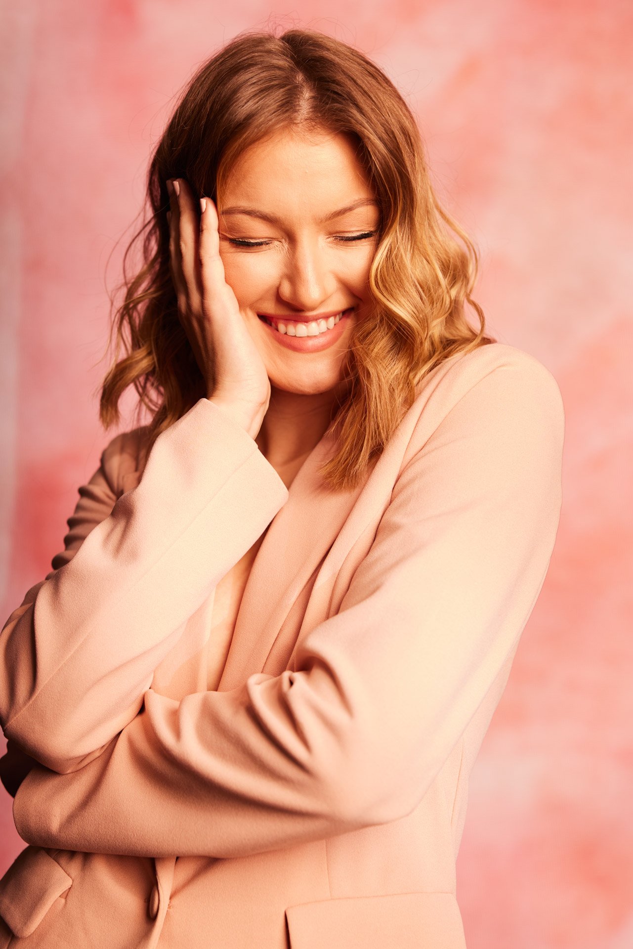 High school senior laughing in a blush blazer against a coral pink studio backdrop
