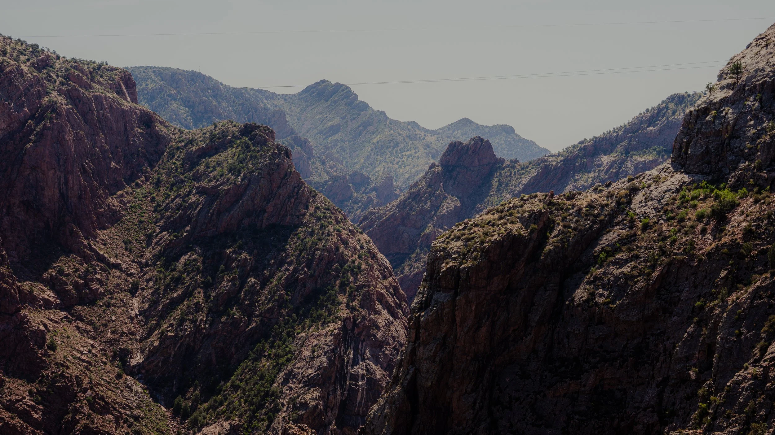 Mountain landscape with rugged, rocky cliffs and sparse vegetation under a clear sky.