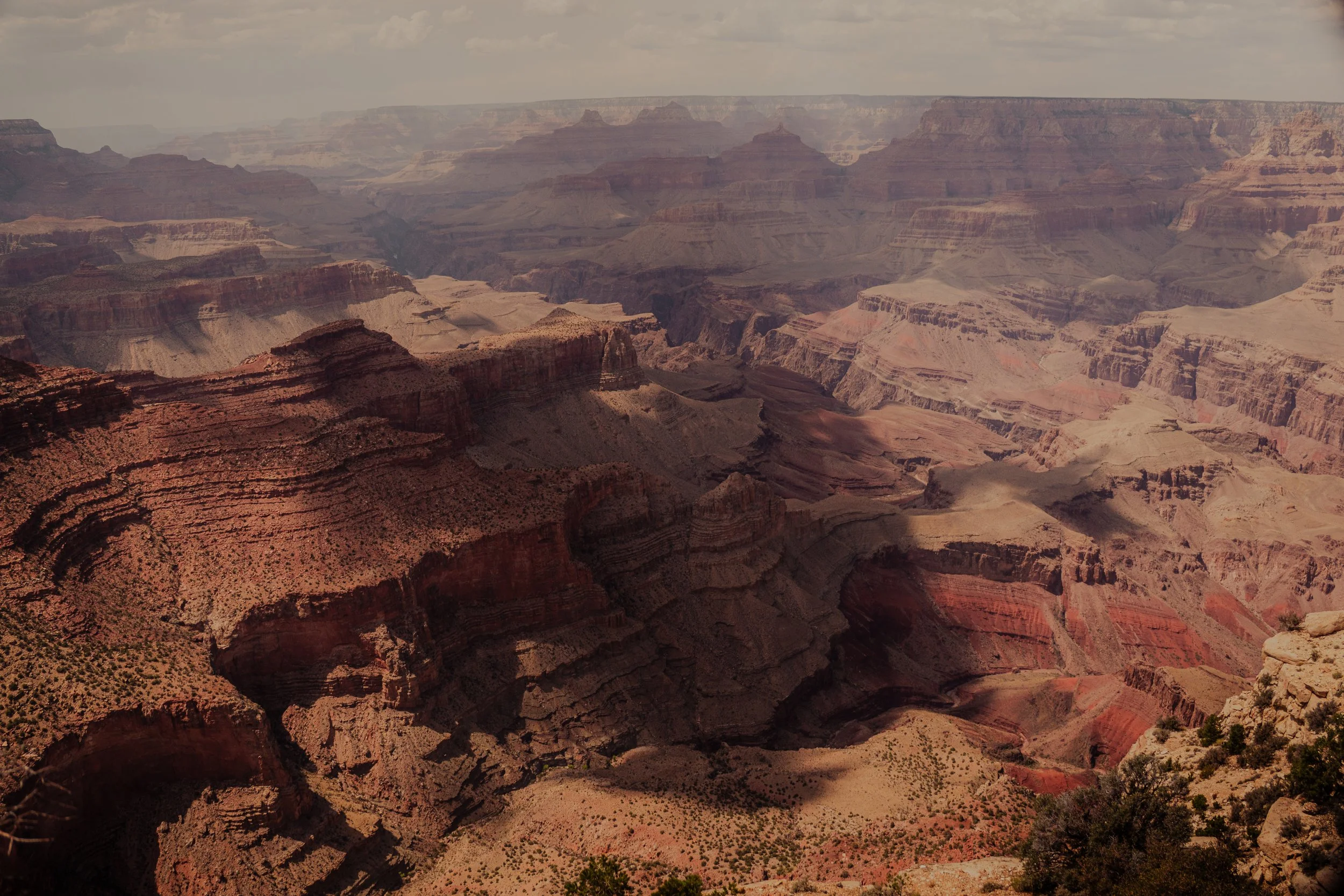 View of the Grand Canyon with layered rock formations and steep cliffs under cloudy sky.