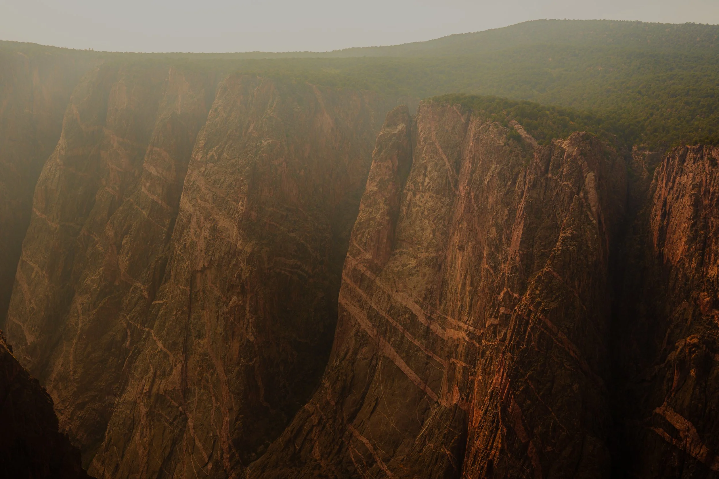 Large canyon with steep, rugged cliffs covered in green vegetation at the top, under a hazy sky.