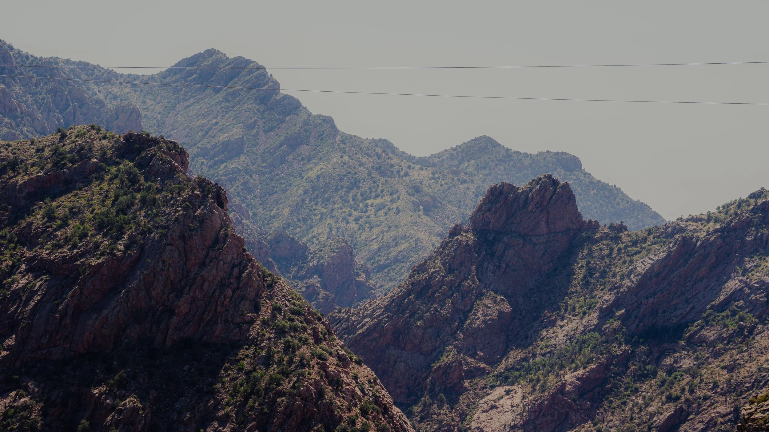 Mountain landscape with rugged, rocky peaks and sparse vegetation under a clear sky.