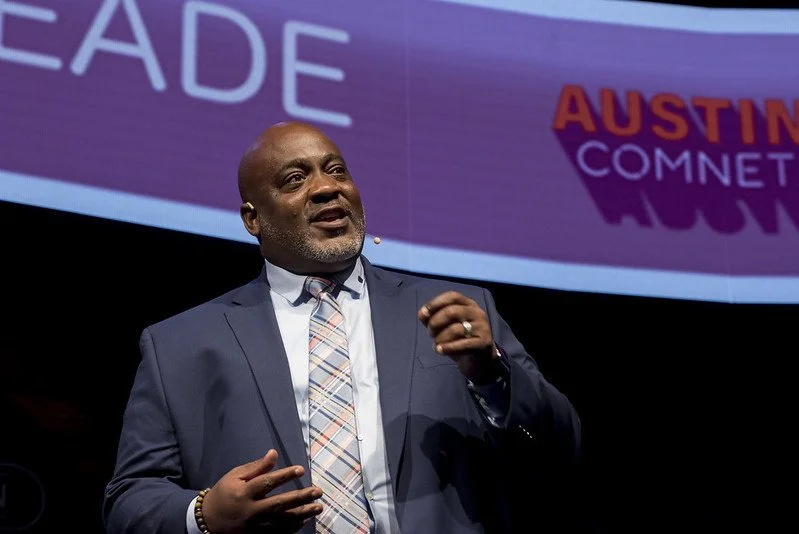 A man speaking on stage wearing a suit.