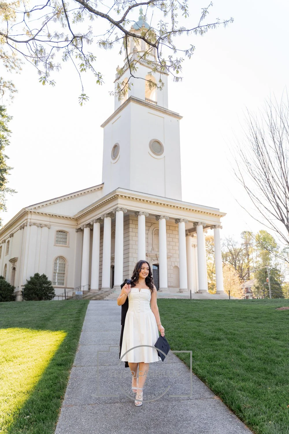 A woman in a white dress walking down a sidewalk in front of a white church with columns and a tall steeple.