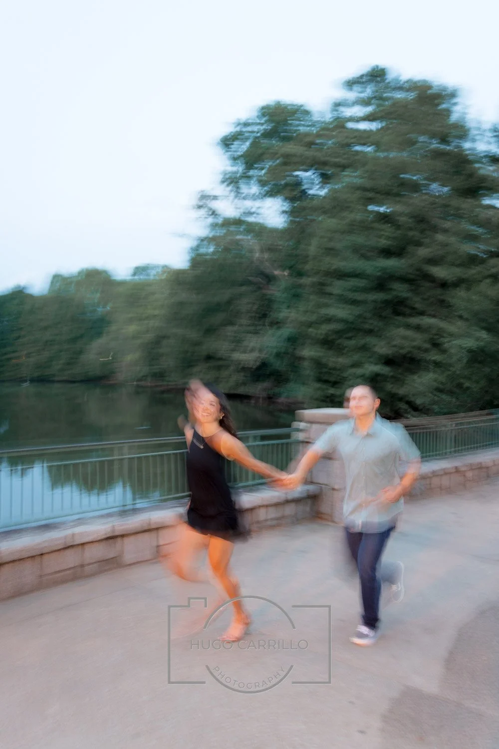 A blurry photo of a man and woman holding hands and running, with trees and a river in the background, during what appears to be dusk.