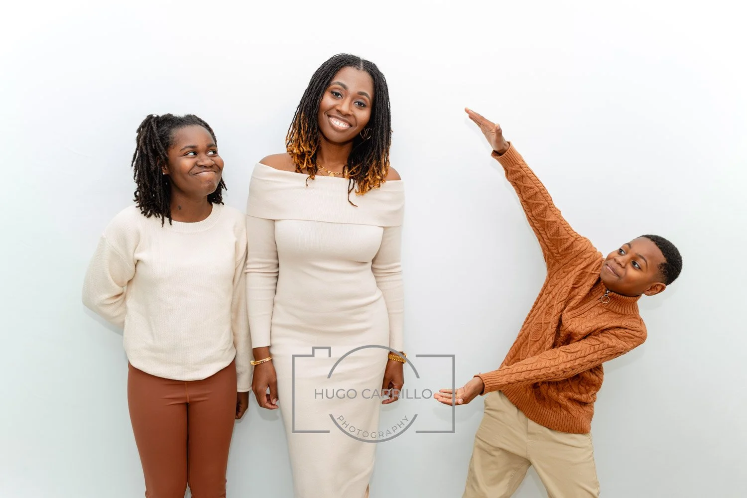 Three people smiling and posing together against a white background, with one person gesturing creatively.
