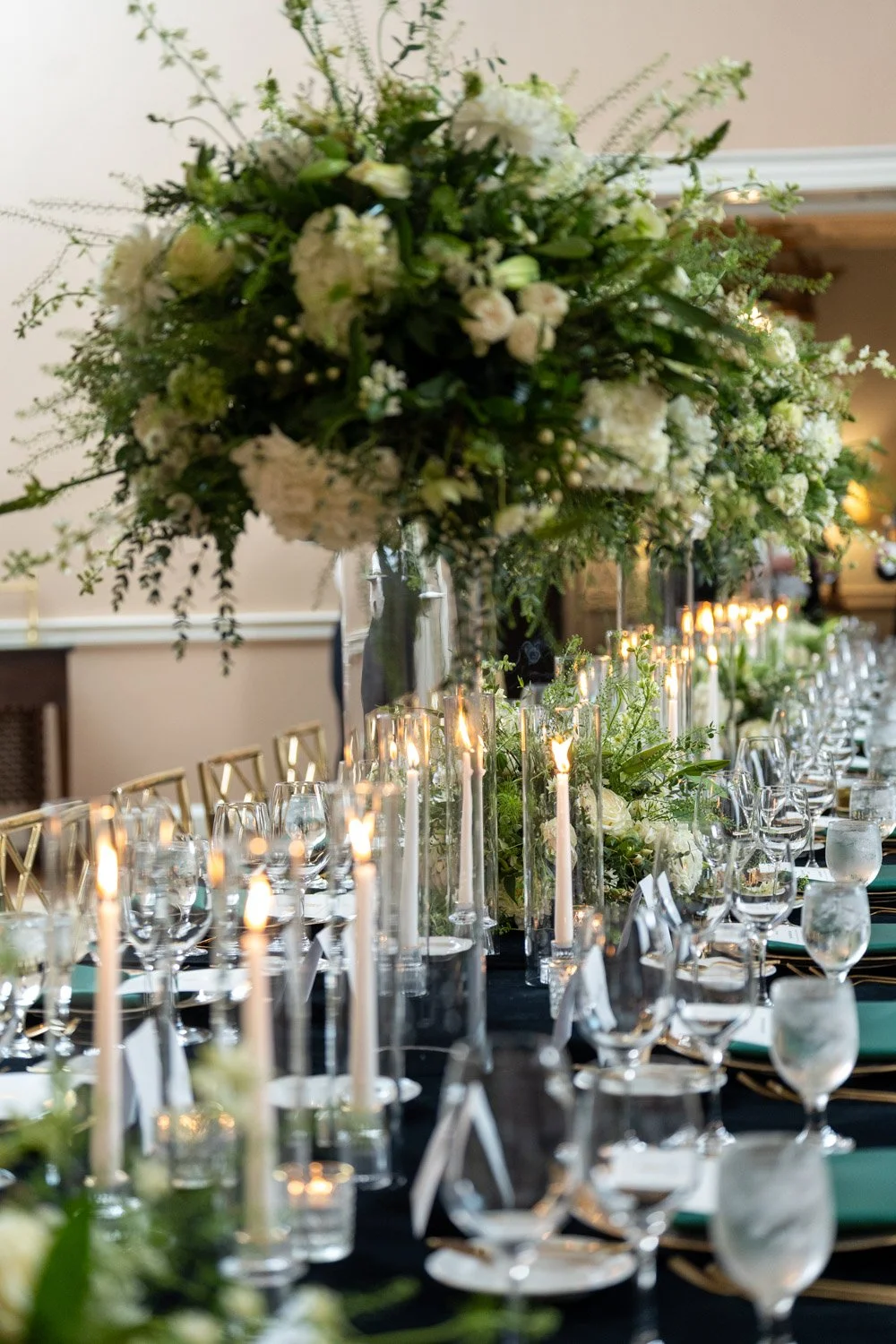 Elegant banquet table with tall floral centerpiece, candlelit votives, and place settings.