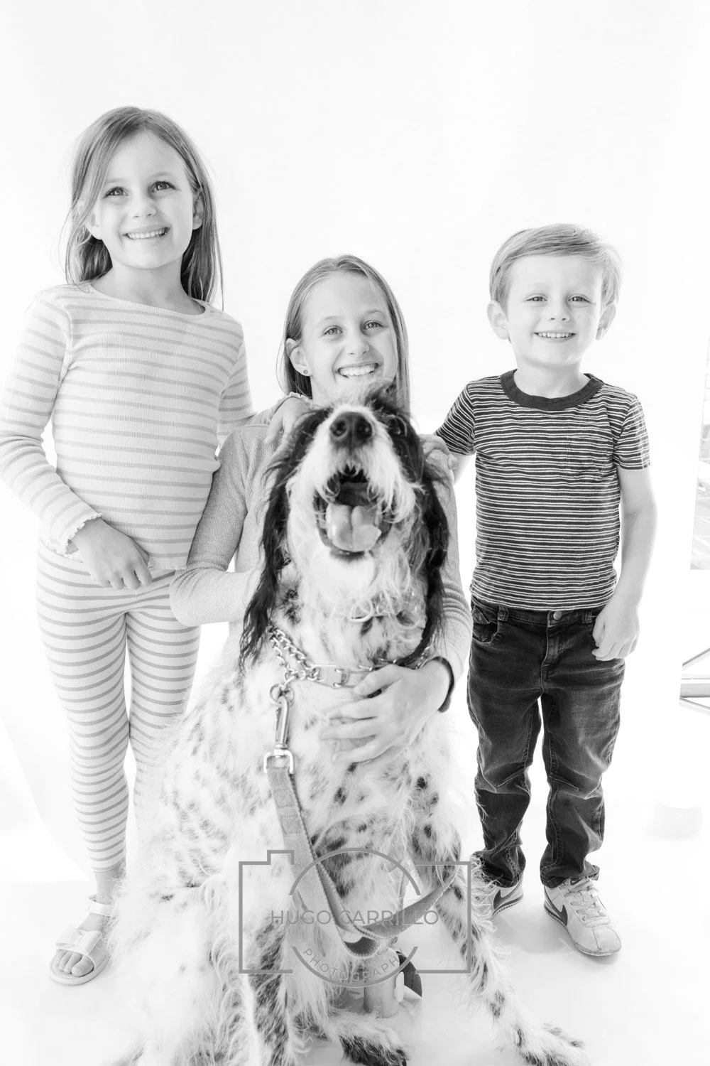 Three children and a woman with their dog in a bright studio with a plain white background.