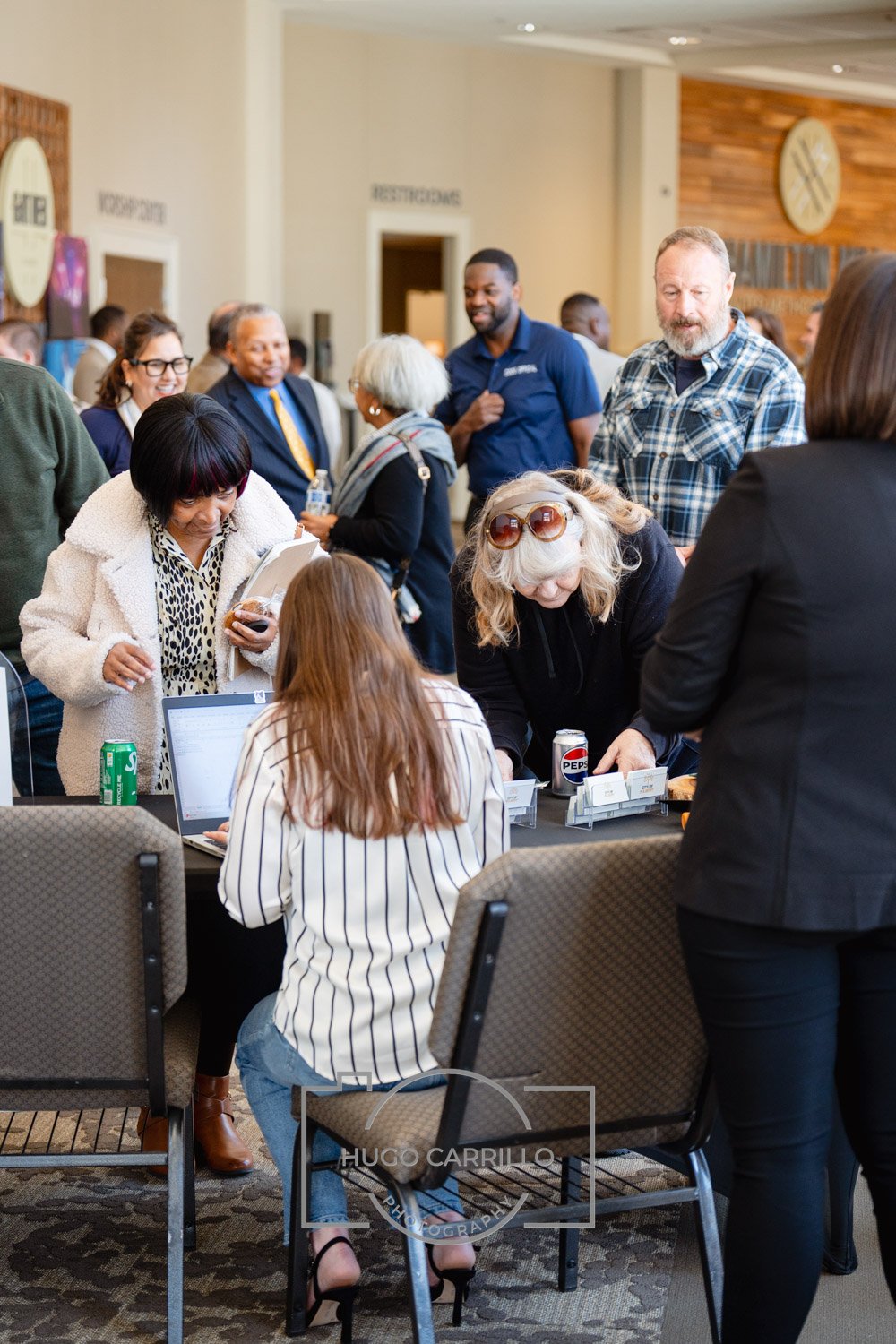 People gathered around a registration or check-in table at a conference or event, with some filling out forms and others chatting in the background.