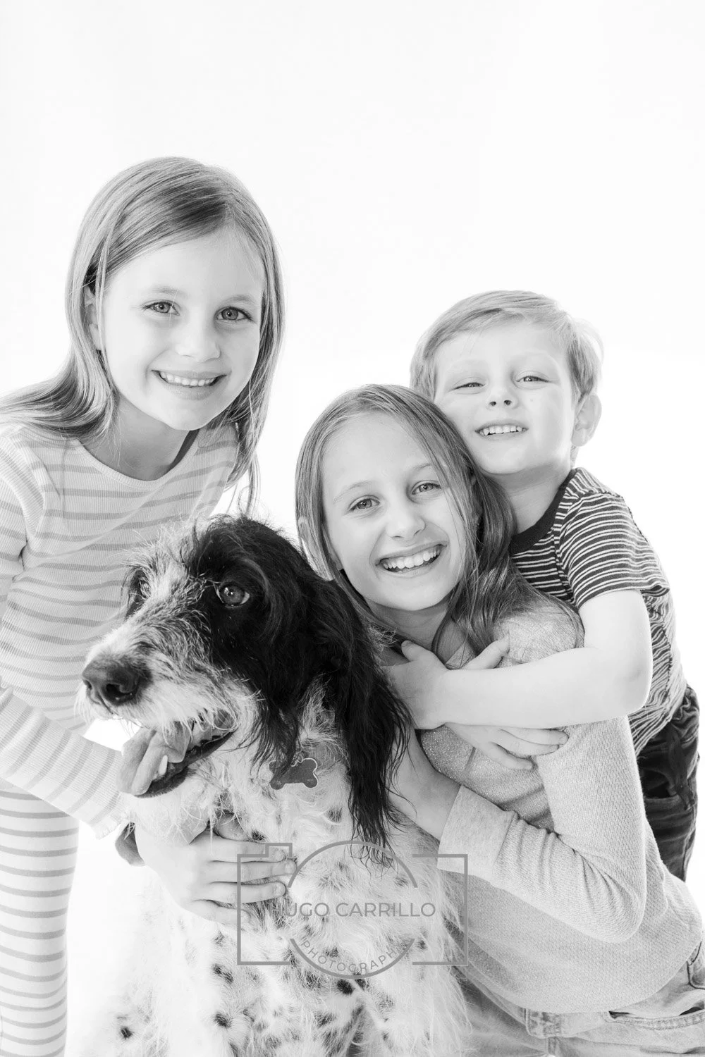 Four children hugging a dog in a group photo, all smiling, in black and white.