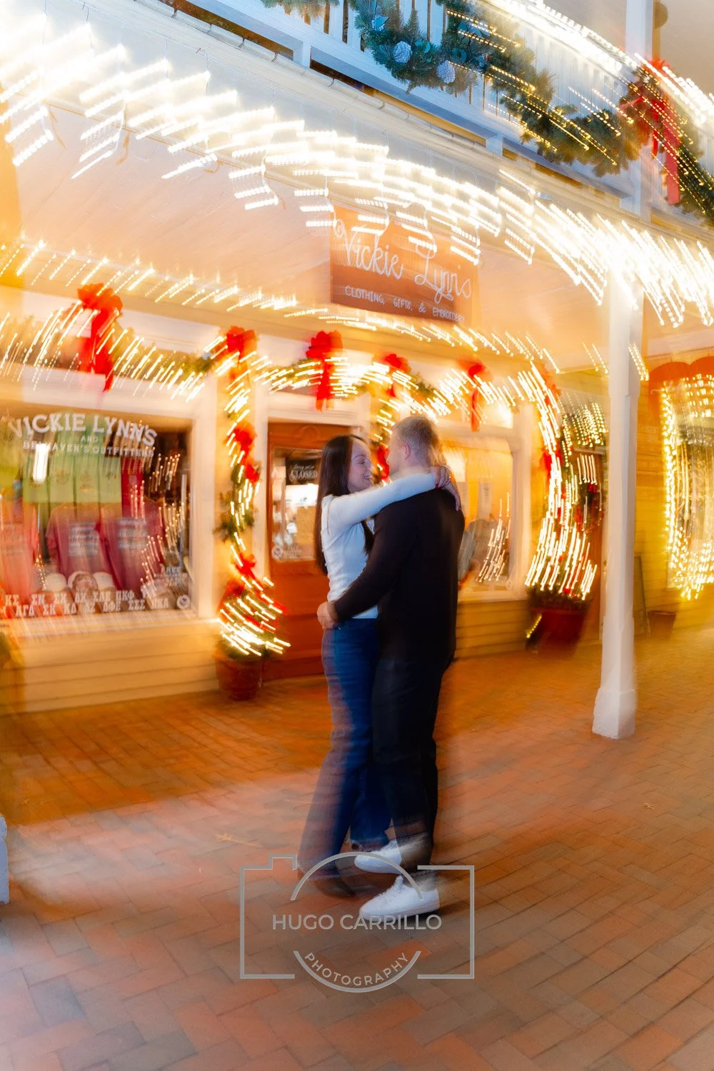 A couple dancing outdoors at night in front of a store decorated with Christmas lights and red ribbons.