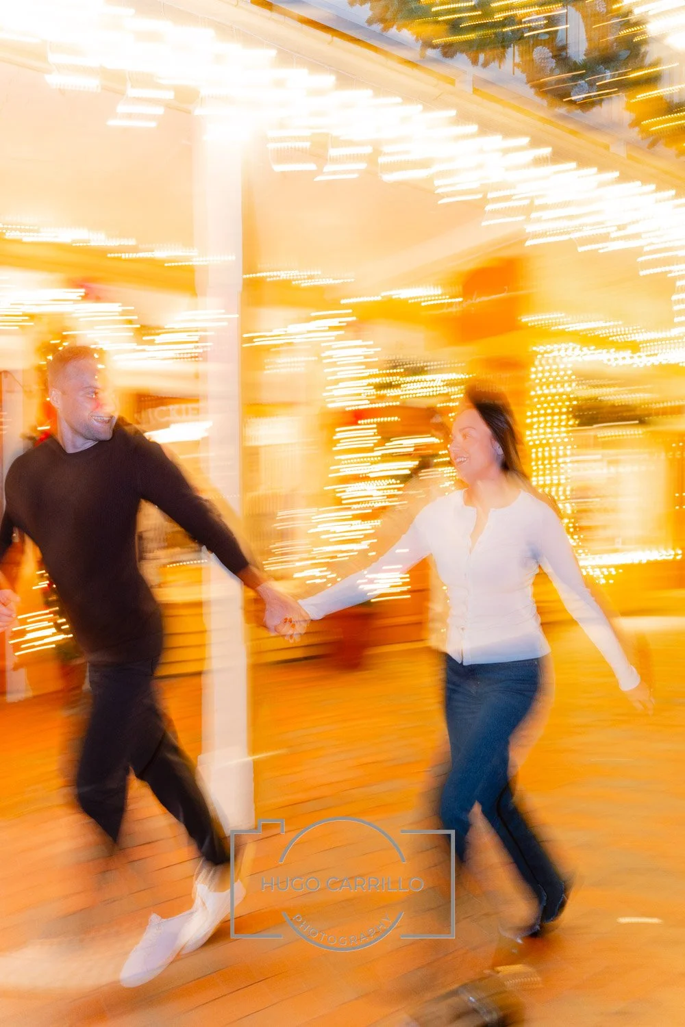 A photo of a smiling man and woman holding hands and dancing at an amusement park or fairground during nighttime, with bright, colorful lights in the background.