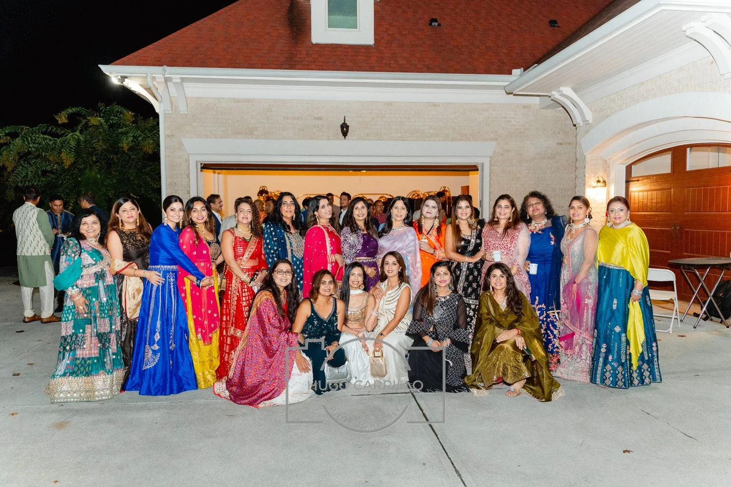 Group of women in colorful traditional Indian attire posing for a photo in front of a house at night.