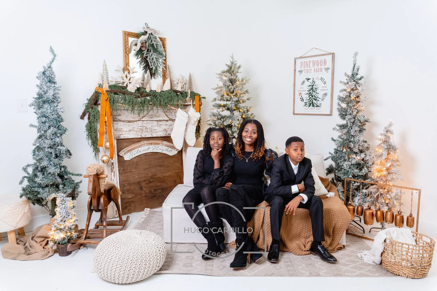 Family of three sitting on a couch in a festive holiday living room, with a Christmas tree, decorated fireplace, and holiday decor.