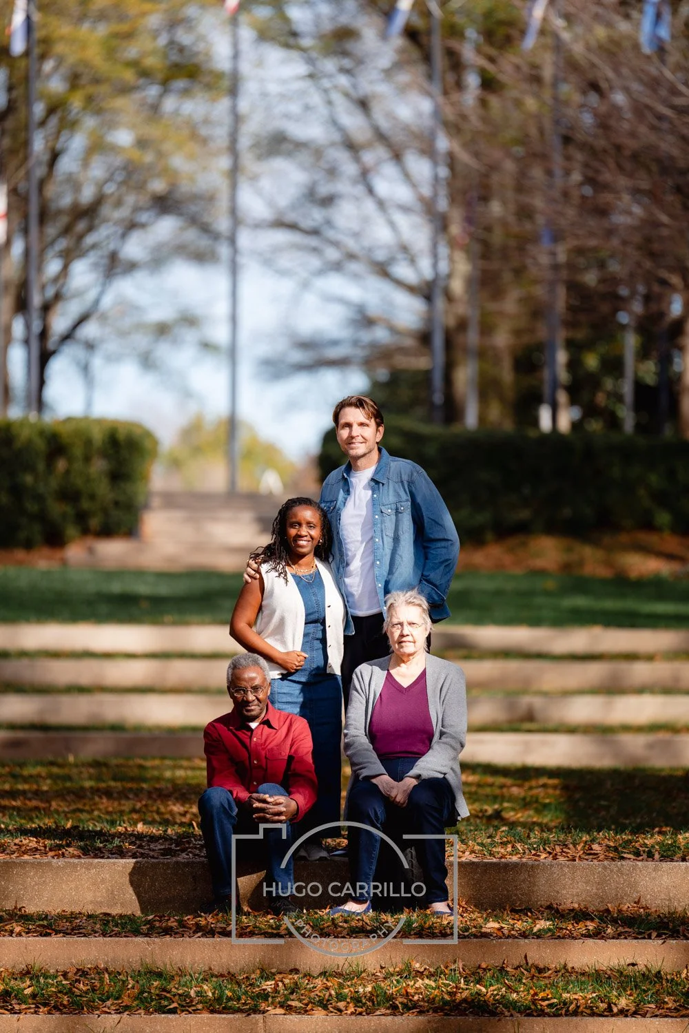 A diverse group of five people posing outdoors on a park staircase during autumn, with trees and blue sky in the background.