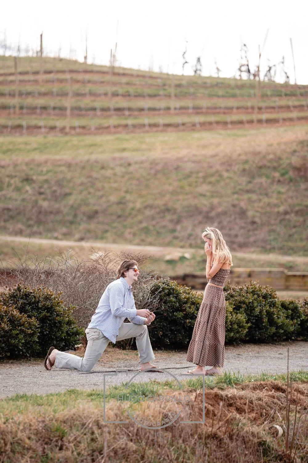A man proposing marriage to a woman outdoors with a scenic landscape in the background.
